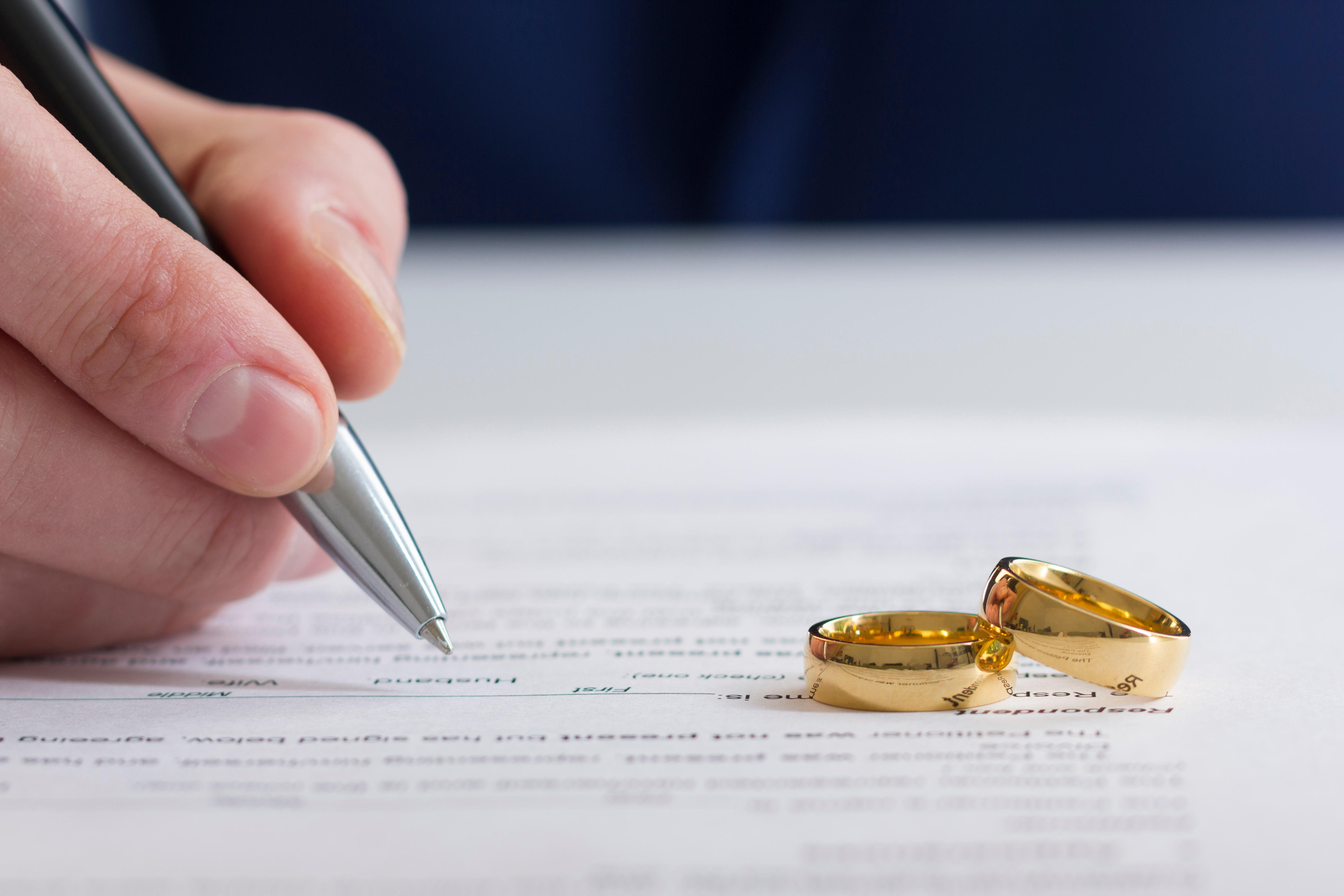 Une main signant des papiers de divorce avec deux bagues sur le dessus | Source : Shutterstock