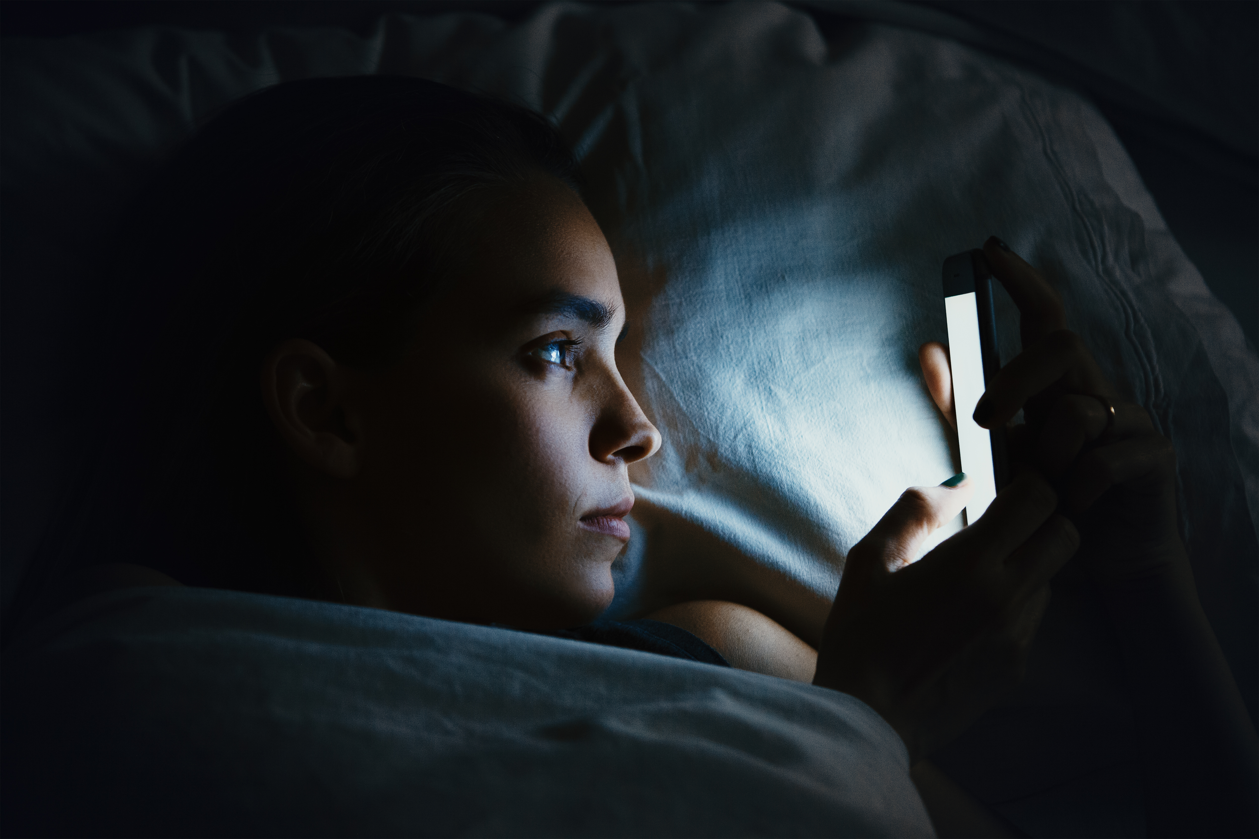 Une jeune femme utilisant un téléphone portable dans un lit | Source : Shutterstock