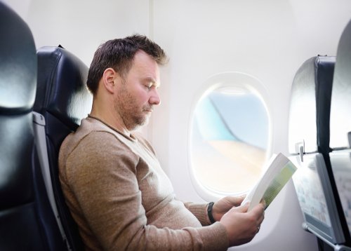 Un homme qui lit pendant son vol dans un avion | Photo : Shutterstock