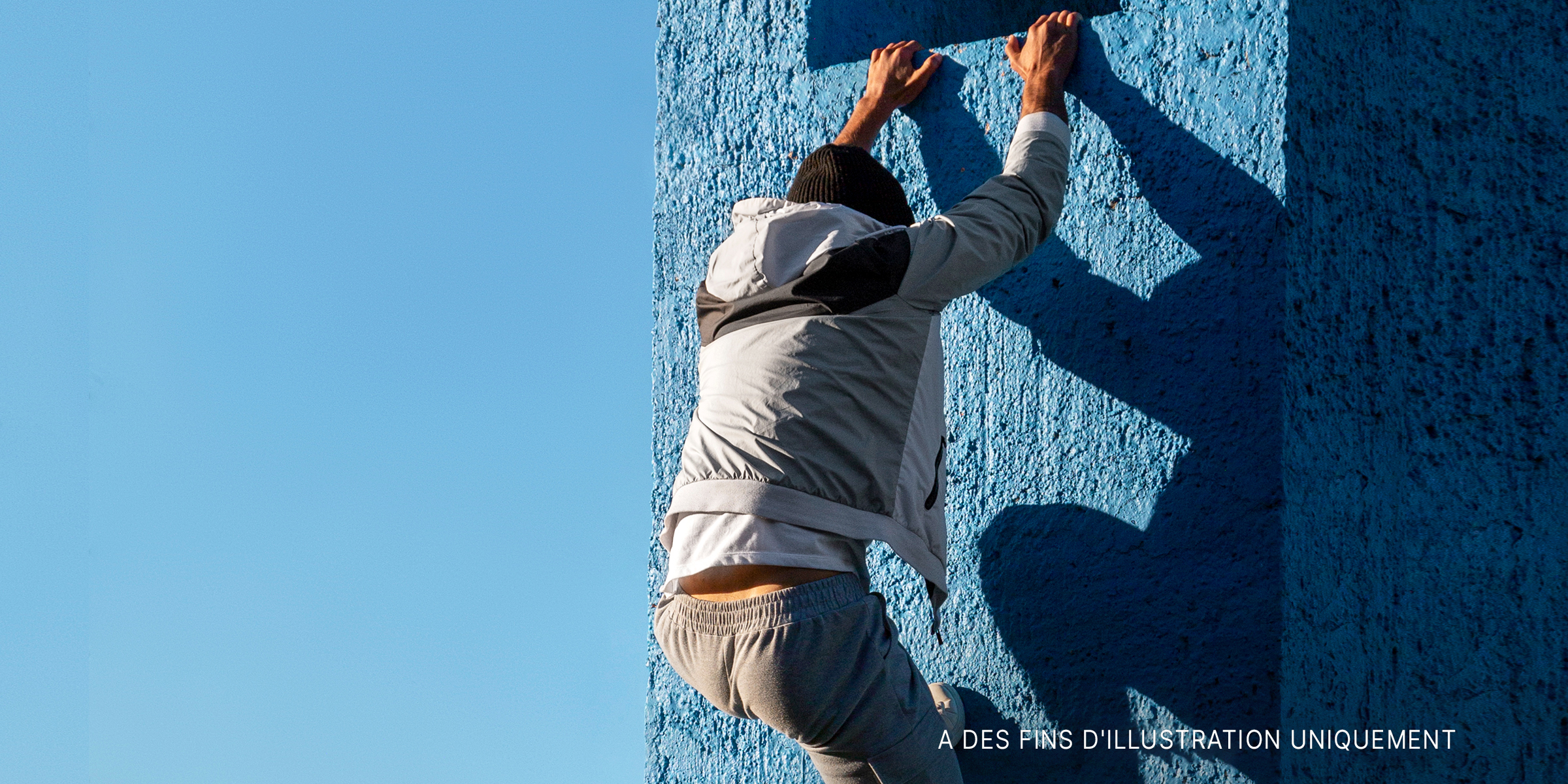 Un homme escaladant un mur bleu | Source : freepik.com