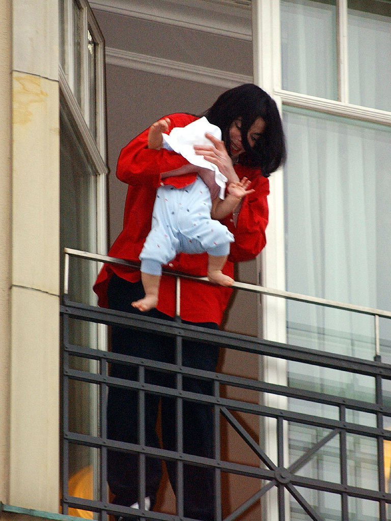 Michael Jackson balance une couverture de 9 mois du balcon de son hôtel en Allemagne en novembre 2002. | Photo : Getty Images