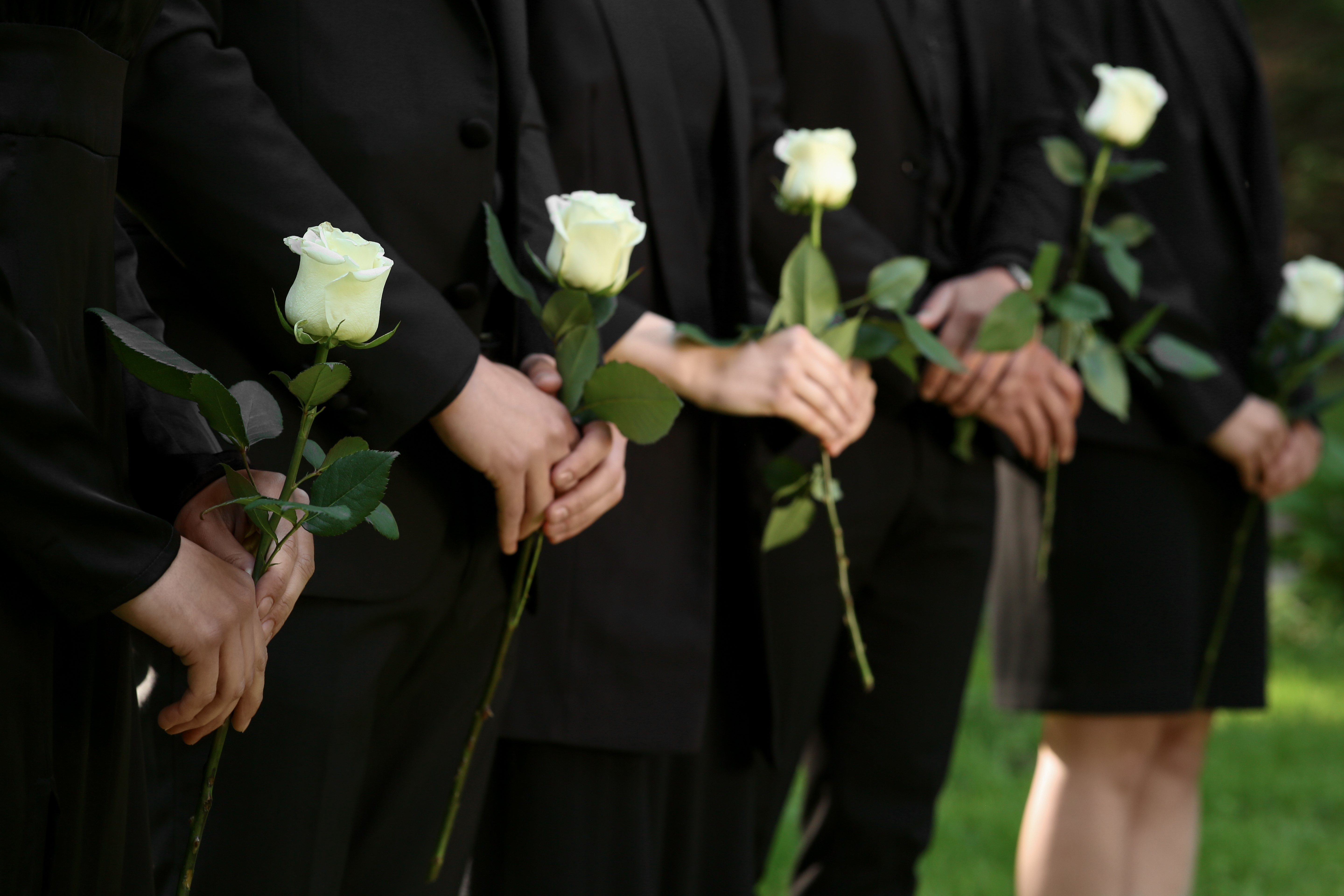 Des personnes à un enterrement tenant des roses blanches | Source : Shutterstock