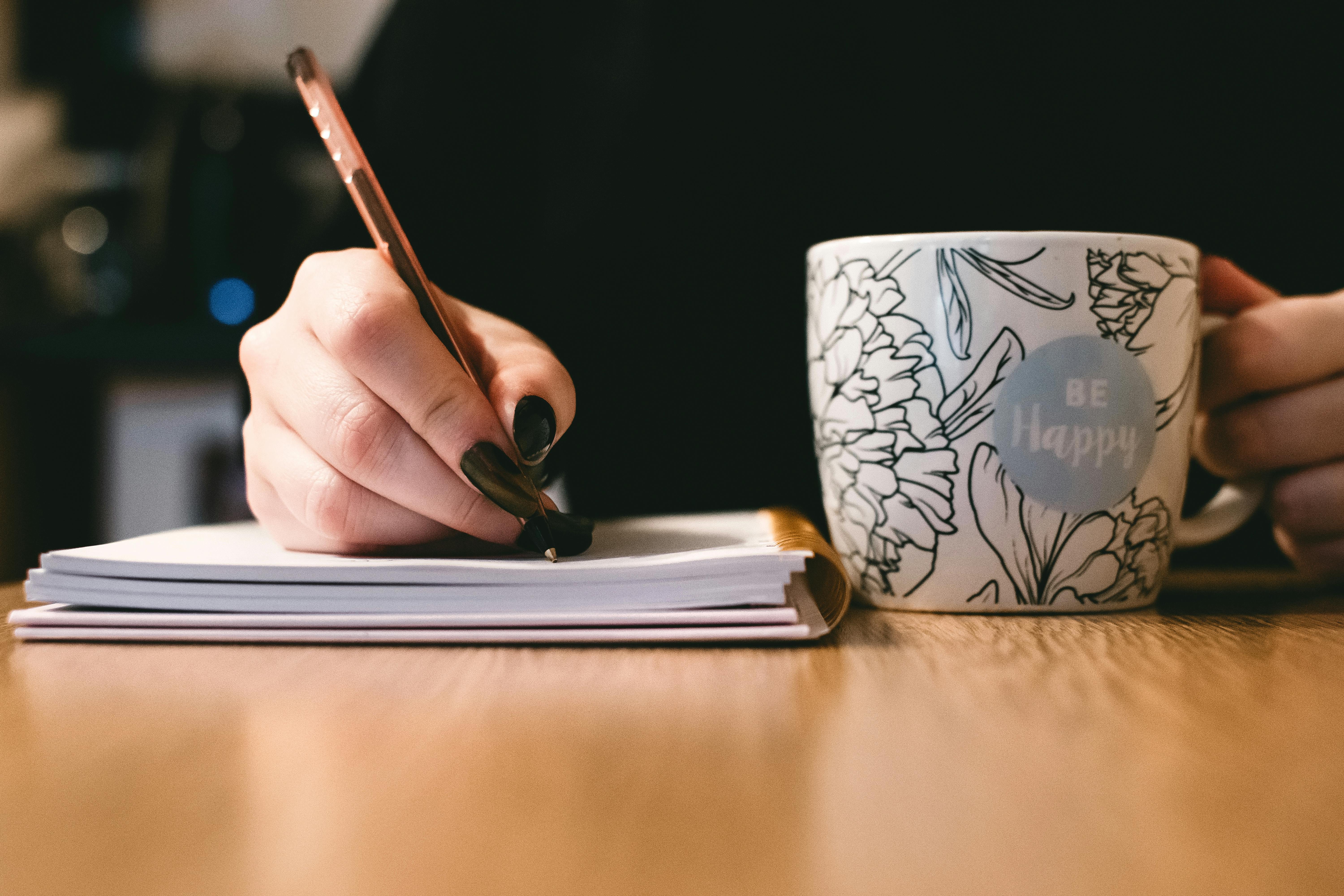 Une femme écrit sur un bloc-notes avec une tasse de café à proximité | Source : Pexels