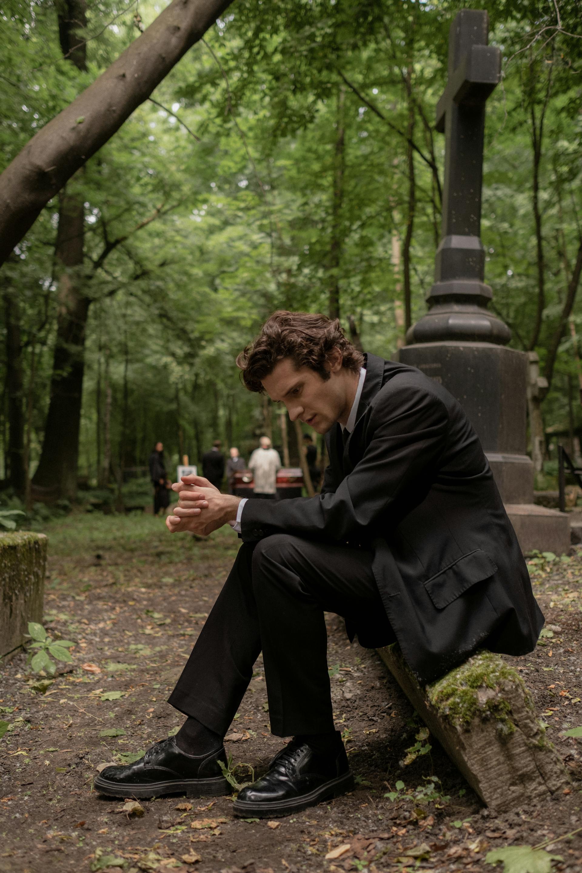 Un homme en costume et veste noirs assis dans un cimetière | Source : Pexels