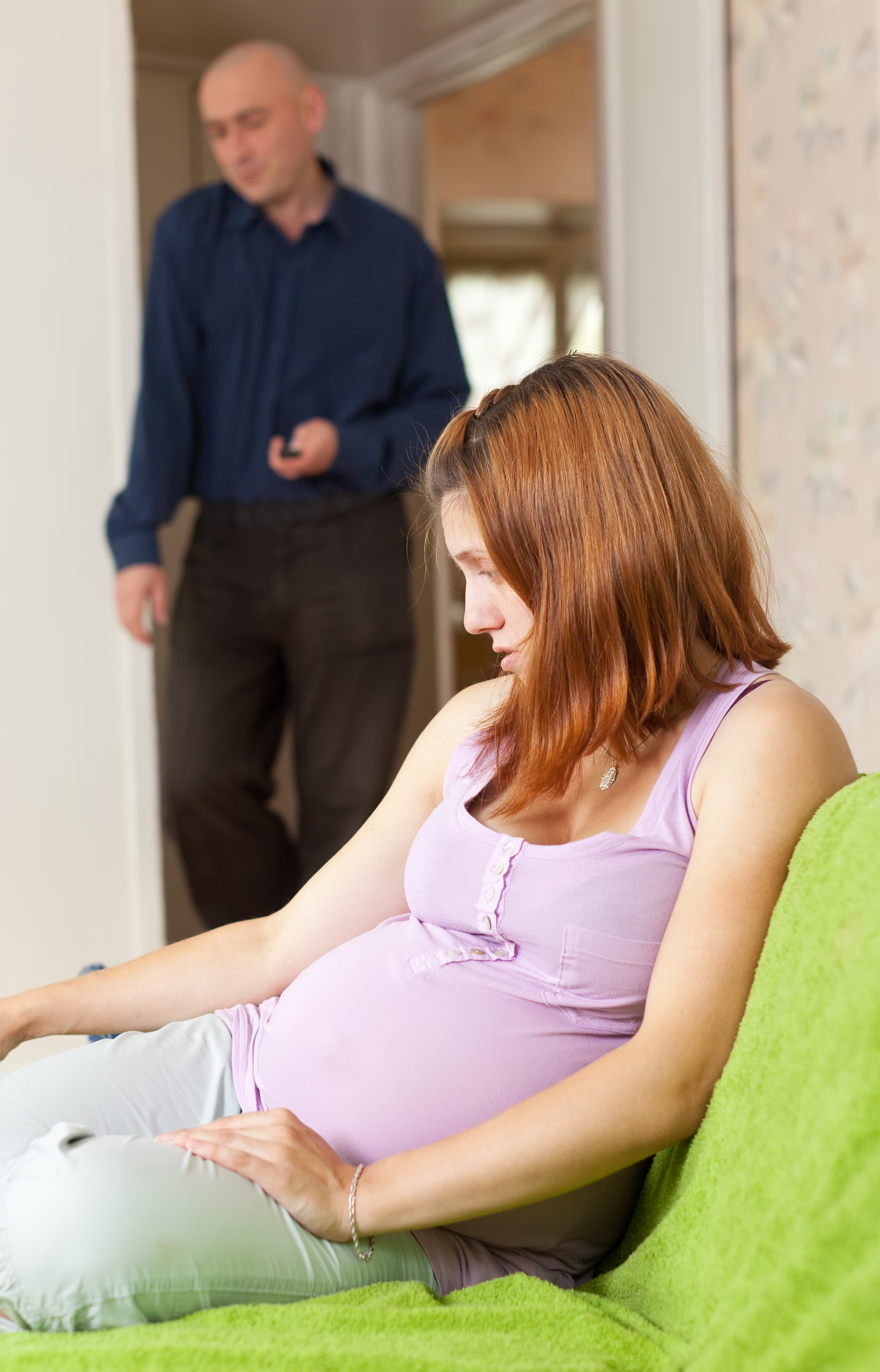 Une femme enceinte qui regarde vers le bas tandis qu'un homme regarde au loin en arrière-plan | Source : Shutterstock