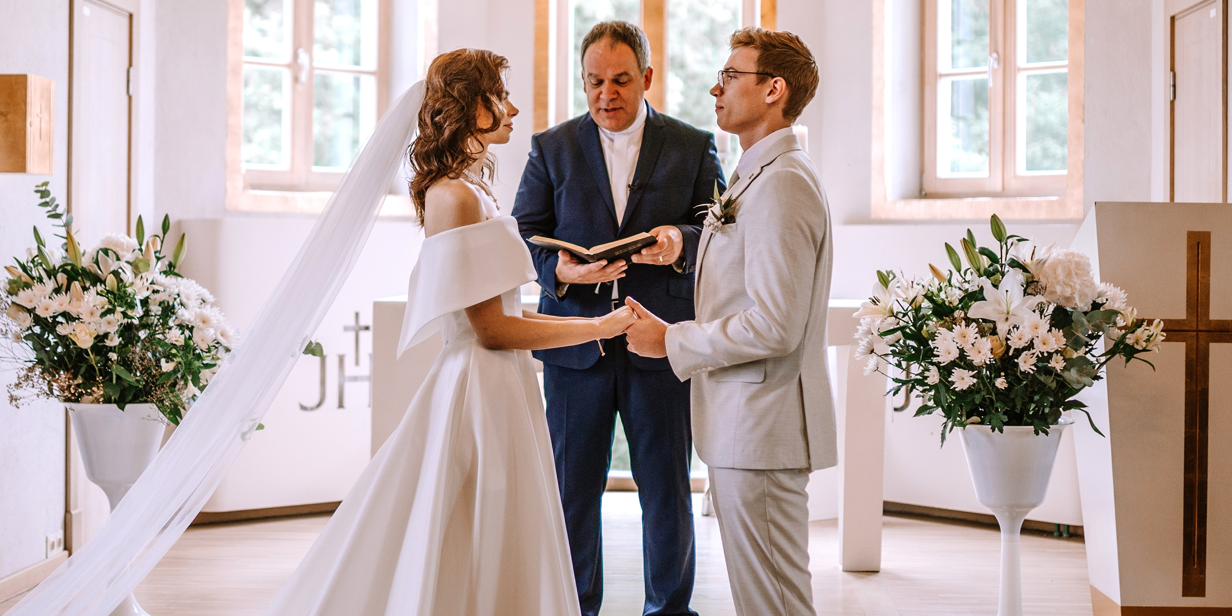 Une mariée et un marié debout devant l'autel se tenant la main pendant qu'un prêtre lit leurs vœux | Source : Shutterstock