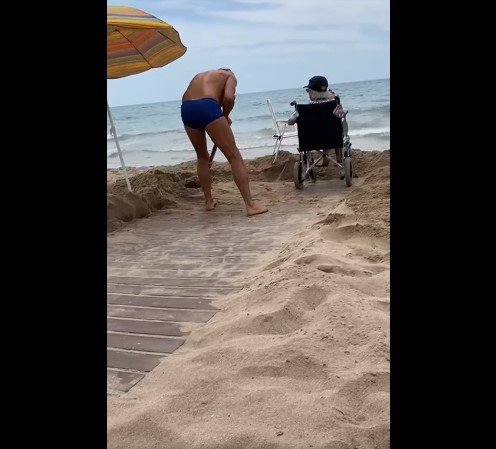 Un fils dégage le sable pour que sa mère puisse atteindre le bord de mer. | Photo : Facebook
