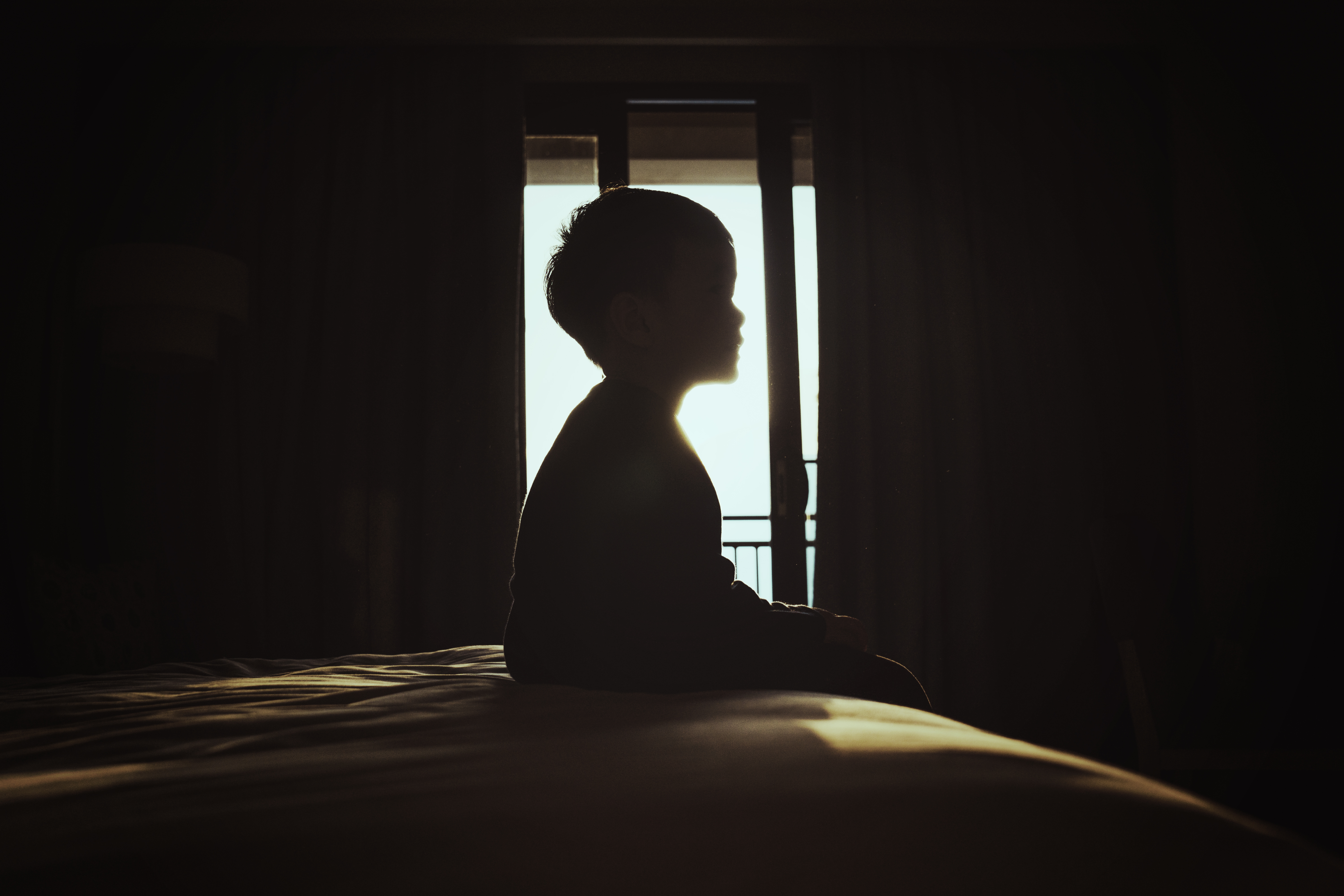 Silhouette d'un garçon assis sur un lit | Source : Getty Images