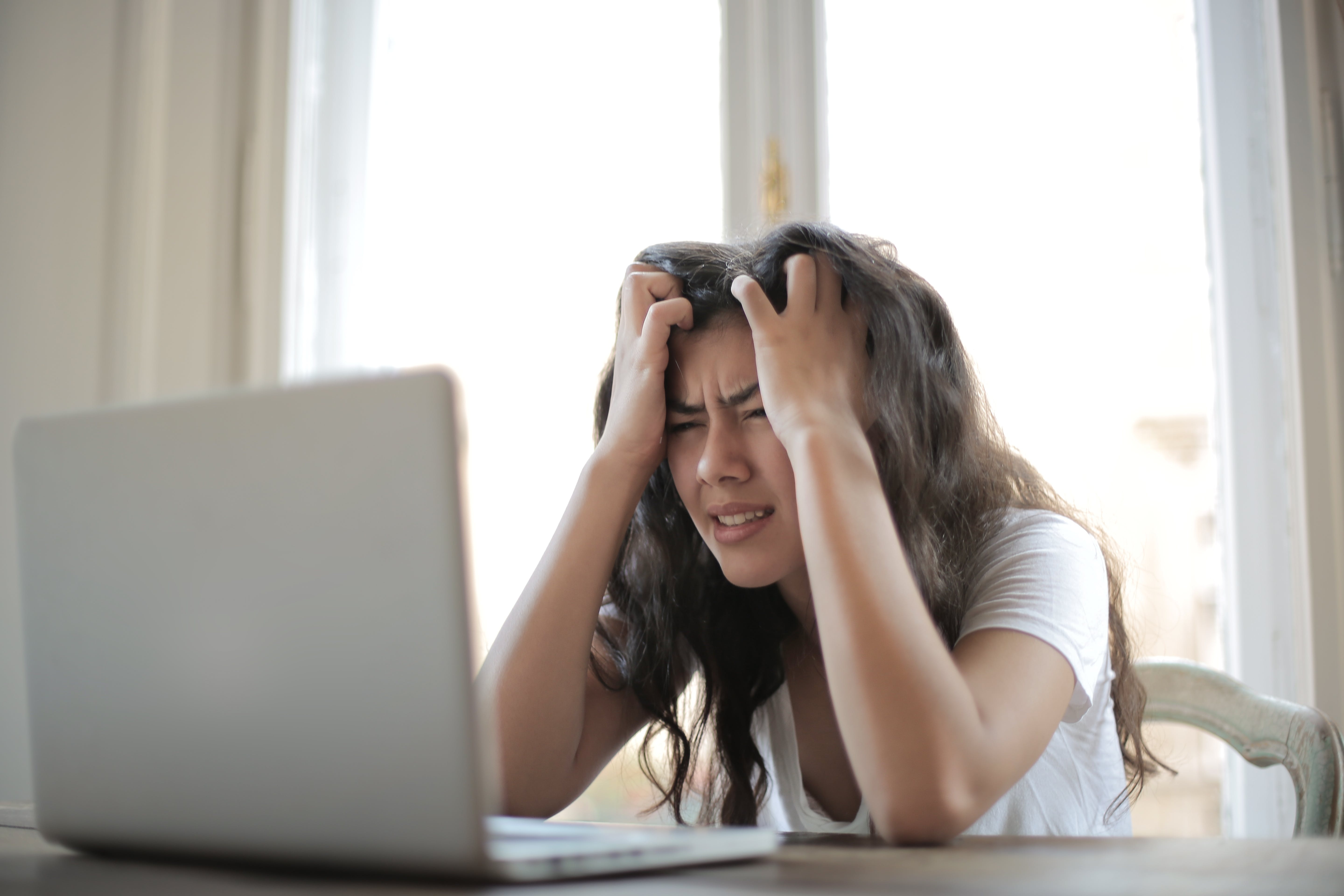 Une femme frustrée se passe les mains dans les cheveux tout en regardant un ordinateur portable | Source : Pexels