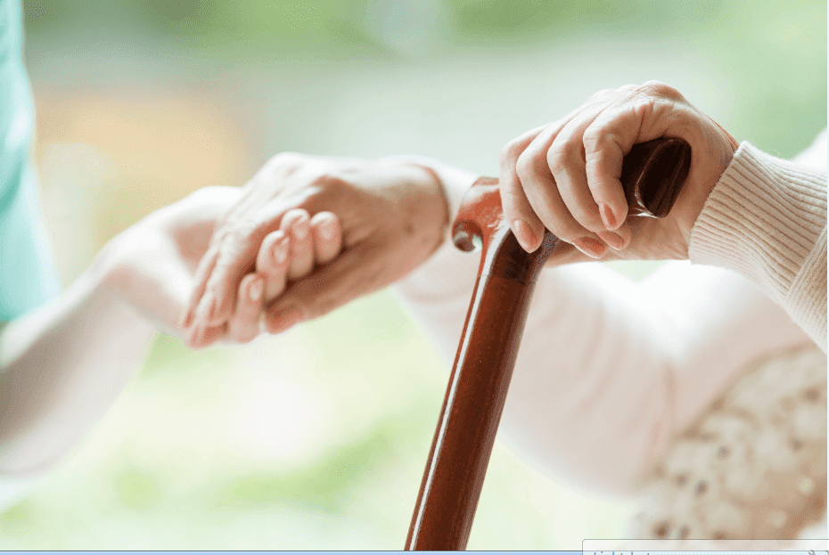 Une personne âgée dépendante ayant une sur sa canne et l'autre dans la main d'une personne plus jeune. | Shutterstock