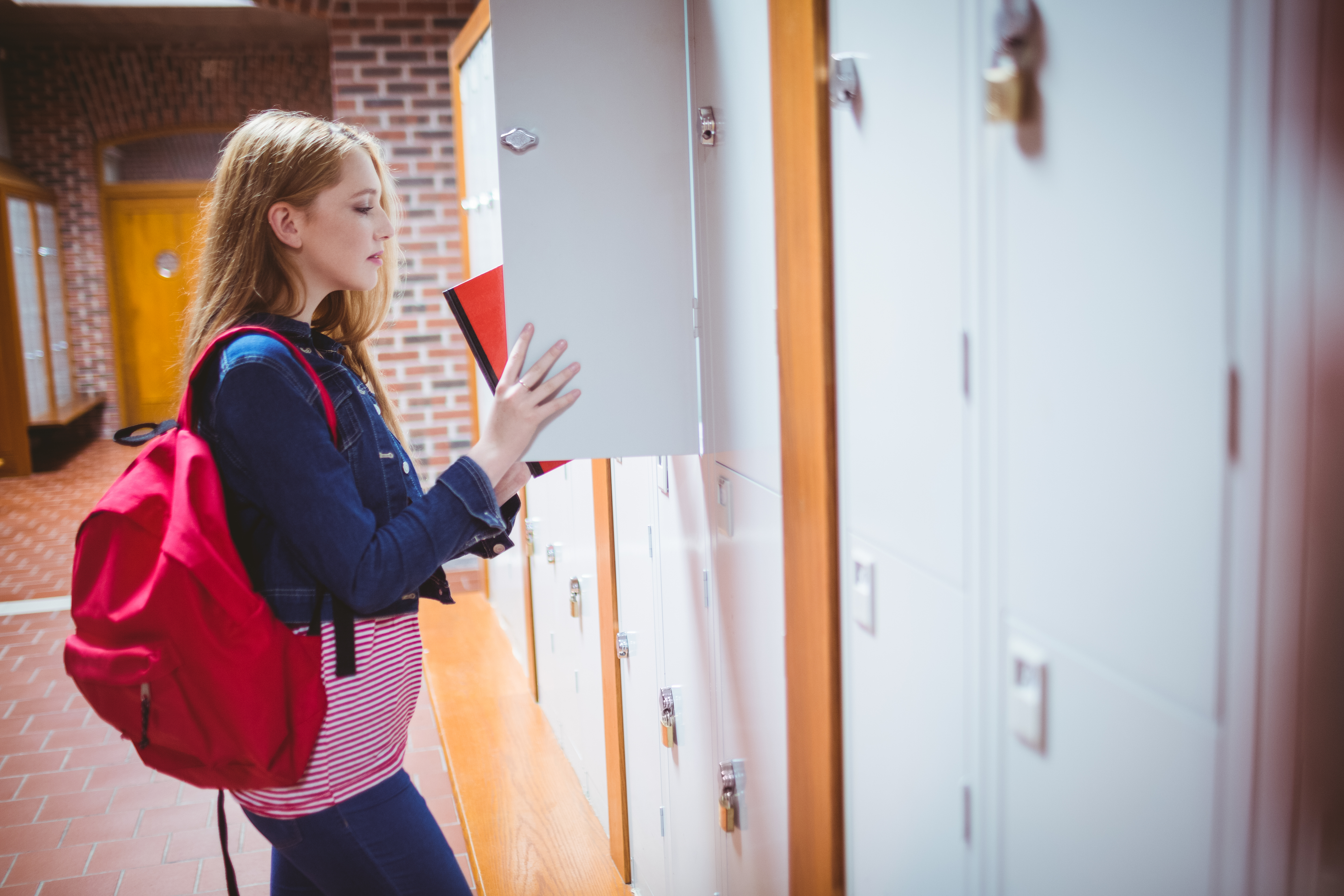 Estudiante con mochila guardando el cuaderno en la taquilla del colegio. | Fuente: Shutterstock