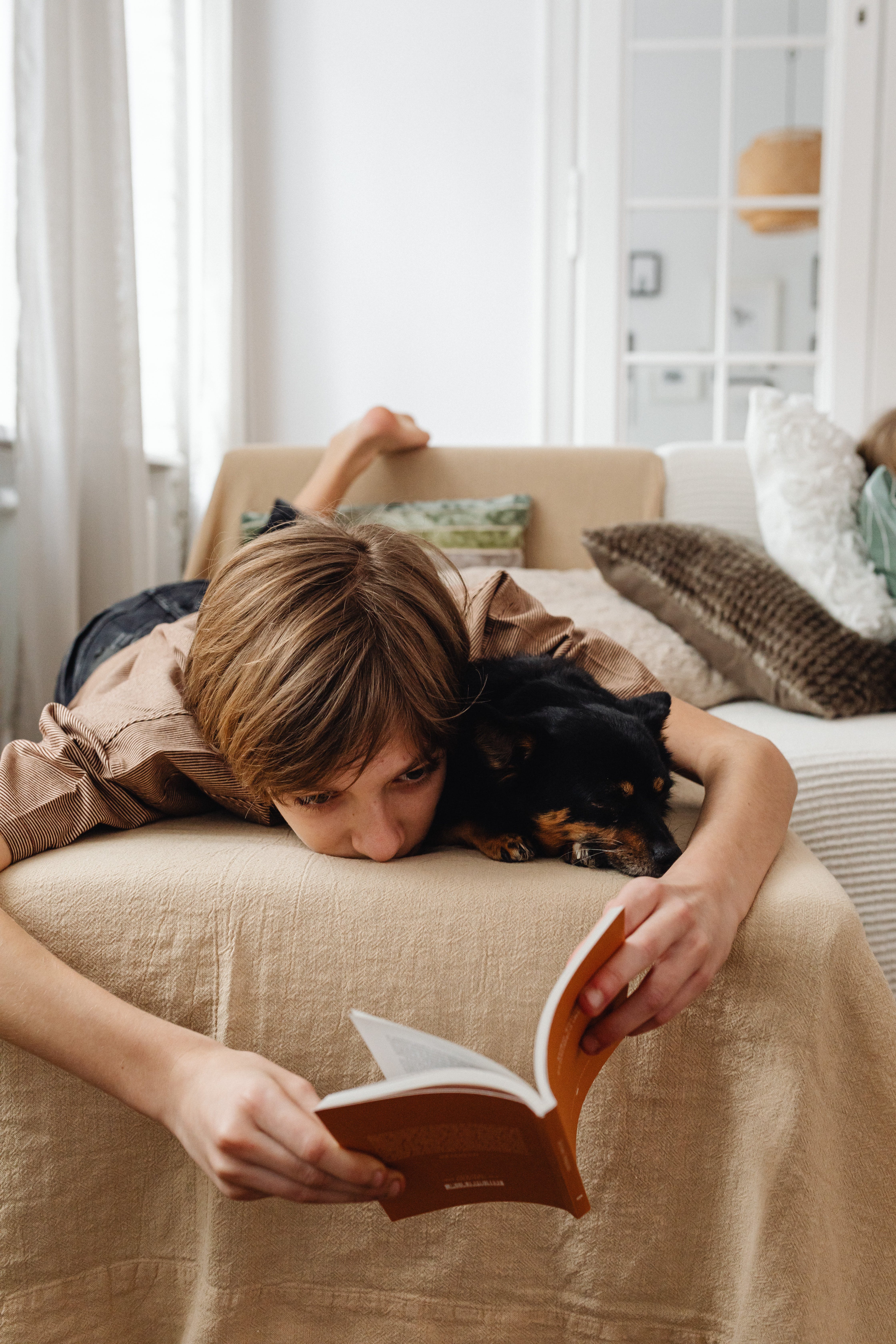 Un petit garçon qui lit un livre avec son chien en étant allongé sur son lit | Source : Pexels