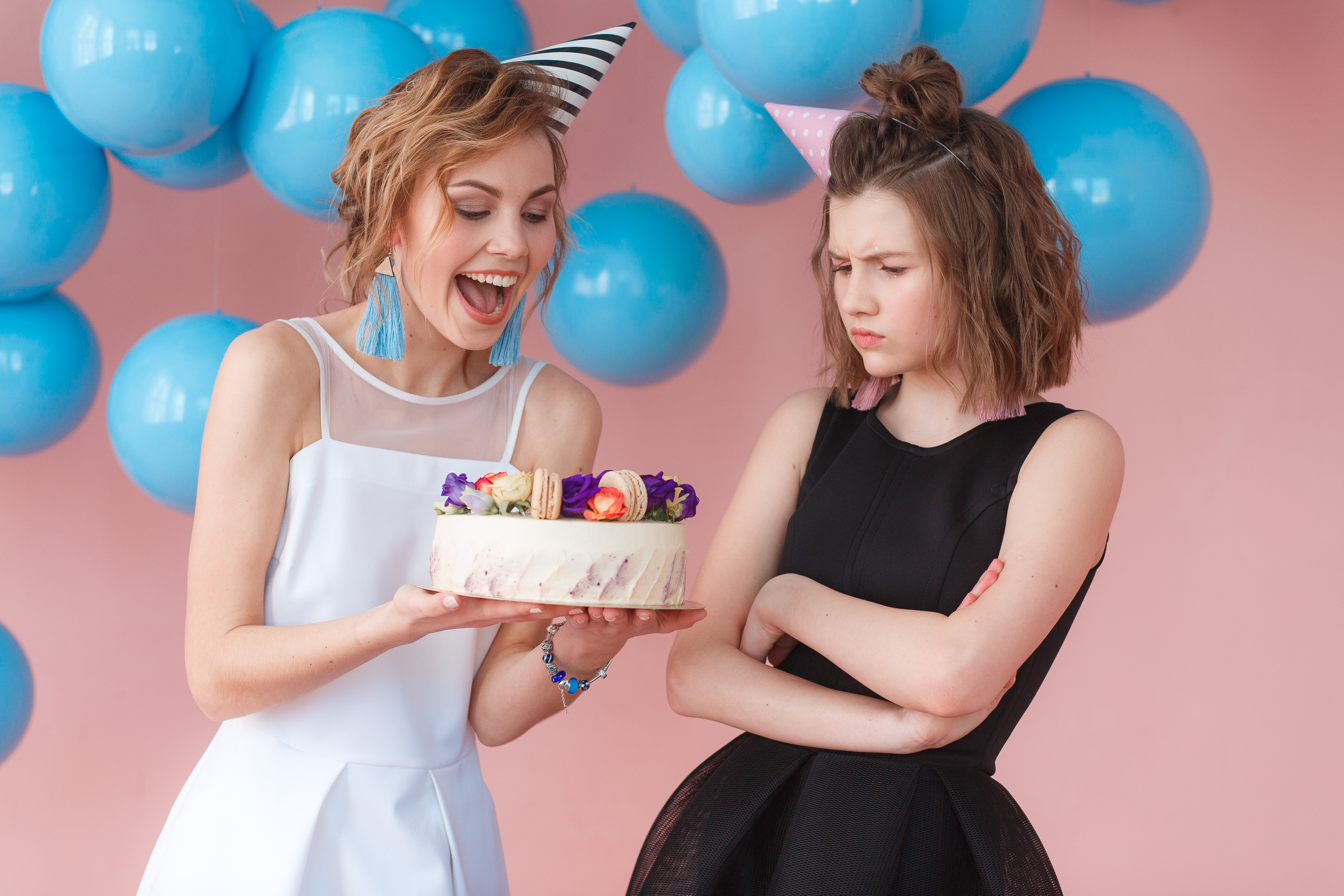 Deux adolescentes tenant un gâteau d'anniversaire, l'une souriant et l'autre fronçant les sourcils | Source : Freepik