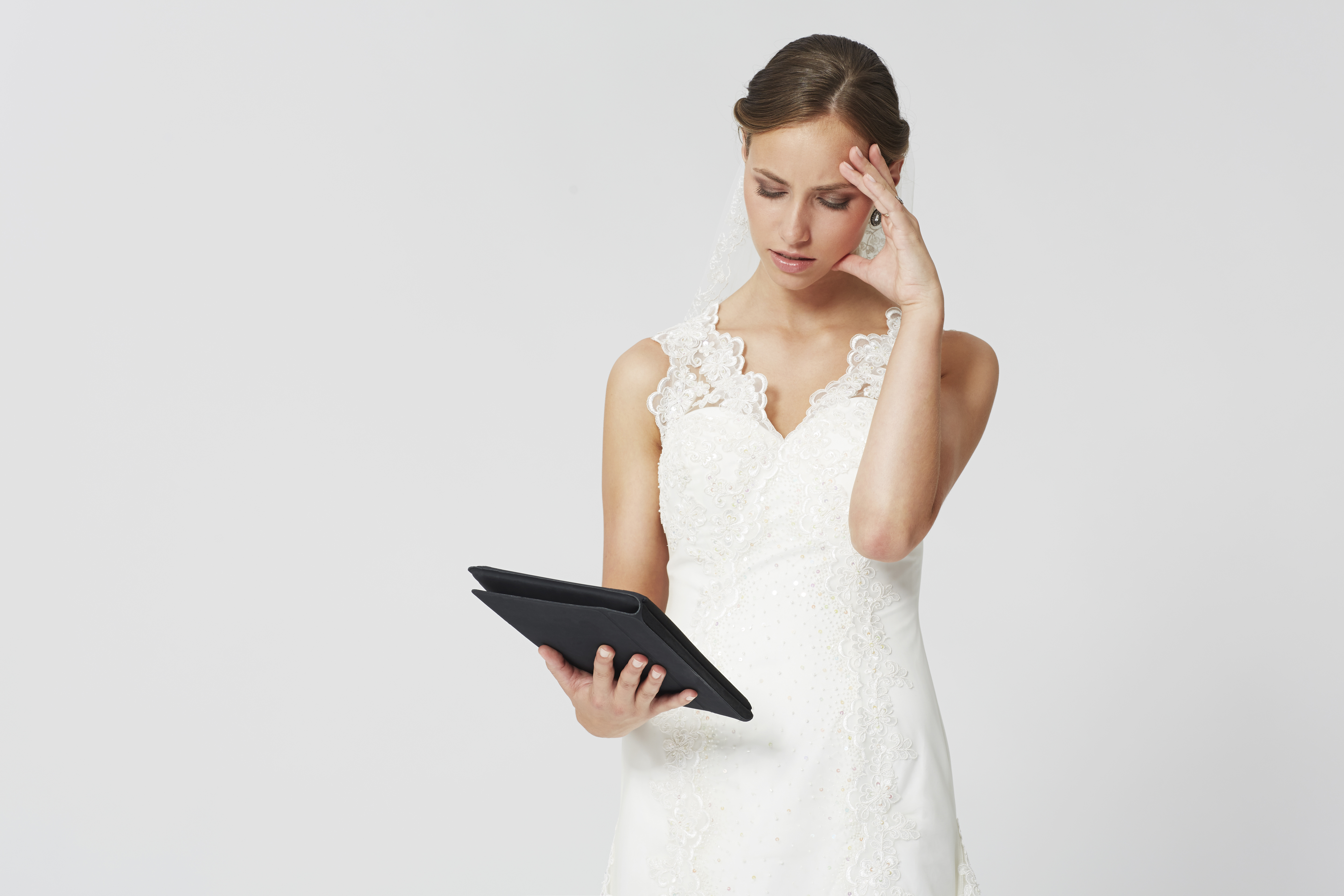 Une femme vêtue d'une robe de mariée blanche a l'air confus tout en tenant une tablette | Source : Shutterstock