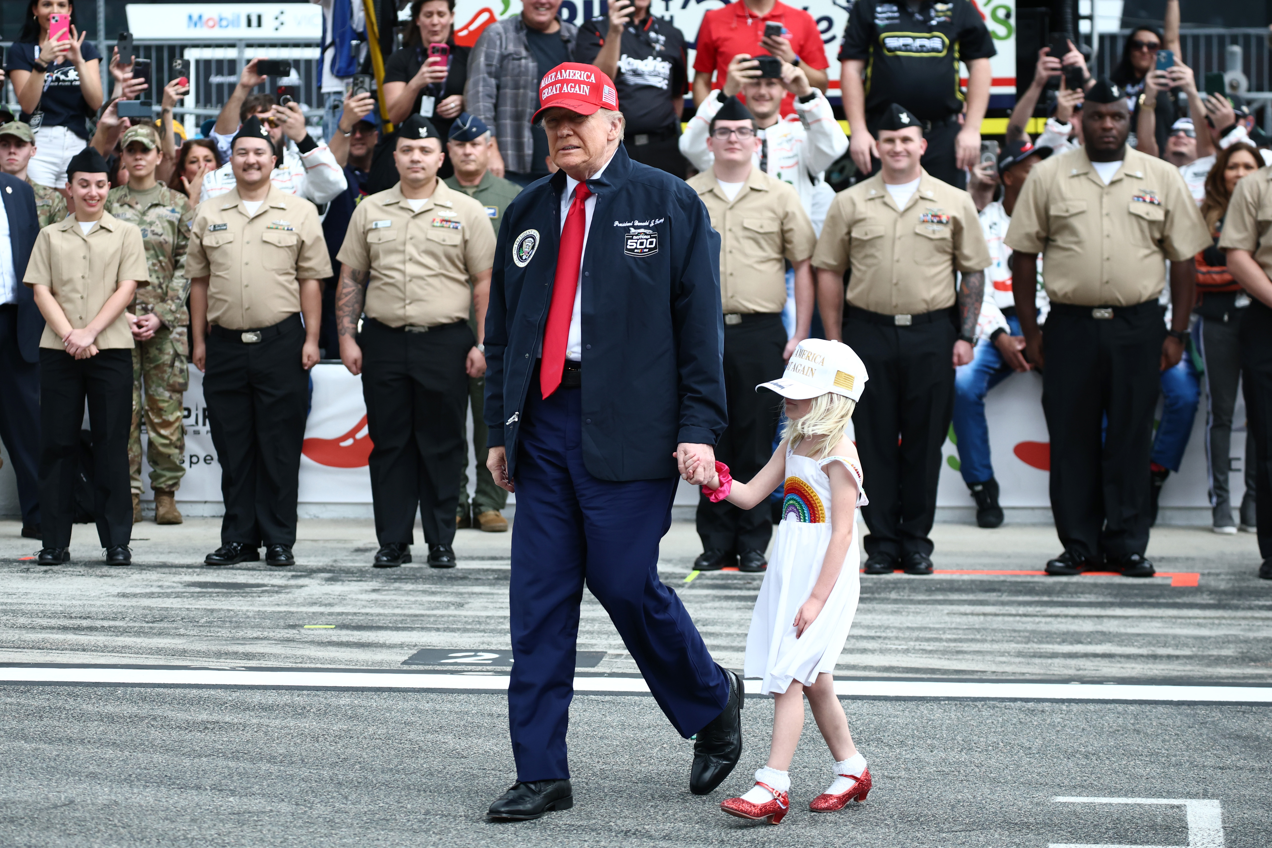 Le président américain Donald Trump et sa petite-fille sont photographiés marchant sur la grille avant la NASCAR Cup Series Daytona 500 au Daytona International Speedway, le 16 février 2025, à Daytona Beach, en Floride | Source : Getty Images