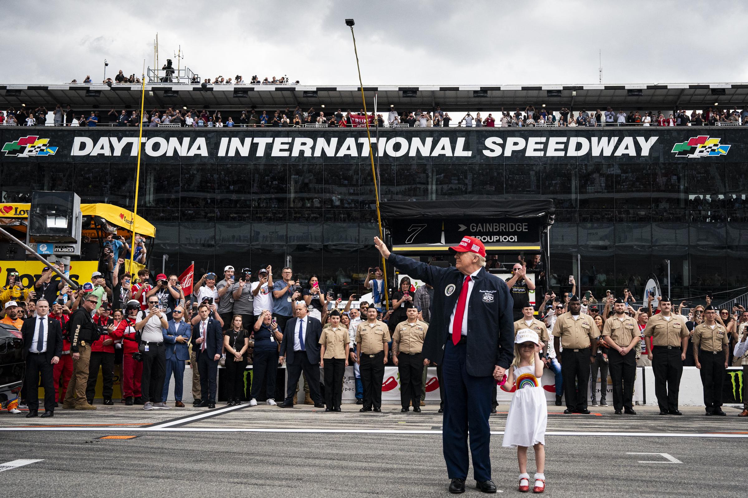 Le président Donald Trump, accompagné de sa petite-fille Carolina Trump, salue les participants avant de monter dans la limousine présidentielle avant le départ de la course de Nascar Daytona 500 au Daytona International Speedway à Daytona Beach, Floride, le 16 février 2025 | Source : Getty Images