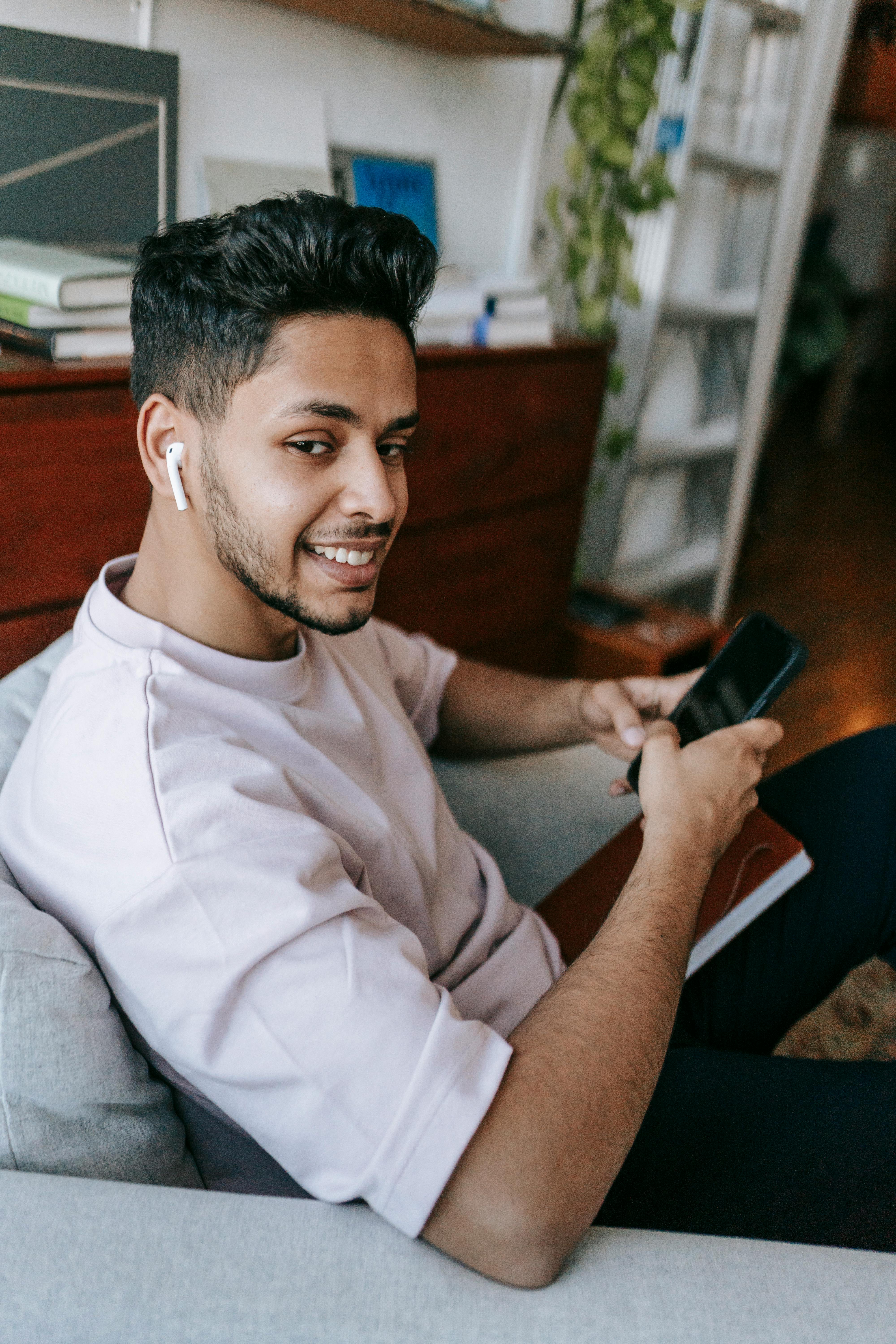 Un homme heureux utilisant son téléphone et des oreillettes | Source : Pexels