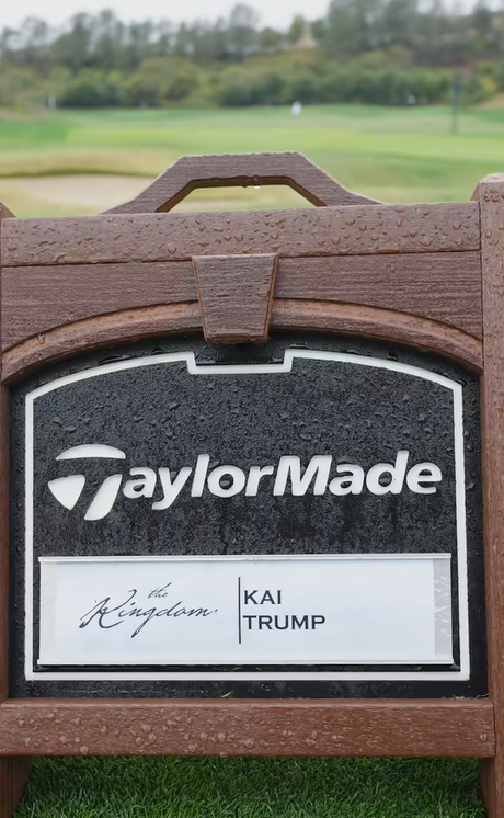 Un panneau TaylorMade portant le nom de Kai Trump se détache sur un fairway flou, parsemé de gouttes de pluie sur son cadre en bois | Source : Tiktok/thekaitrumpgolfer