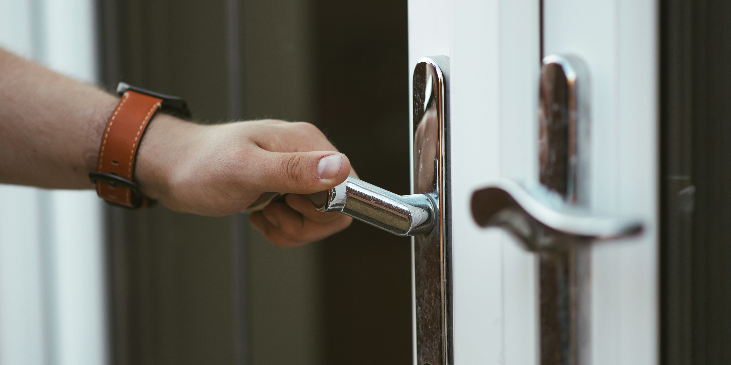 La main d'un homme saisissant une poignée de porte en argent | Source : Shutterstock