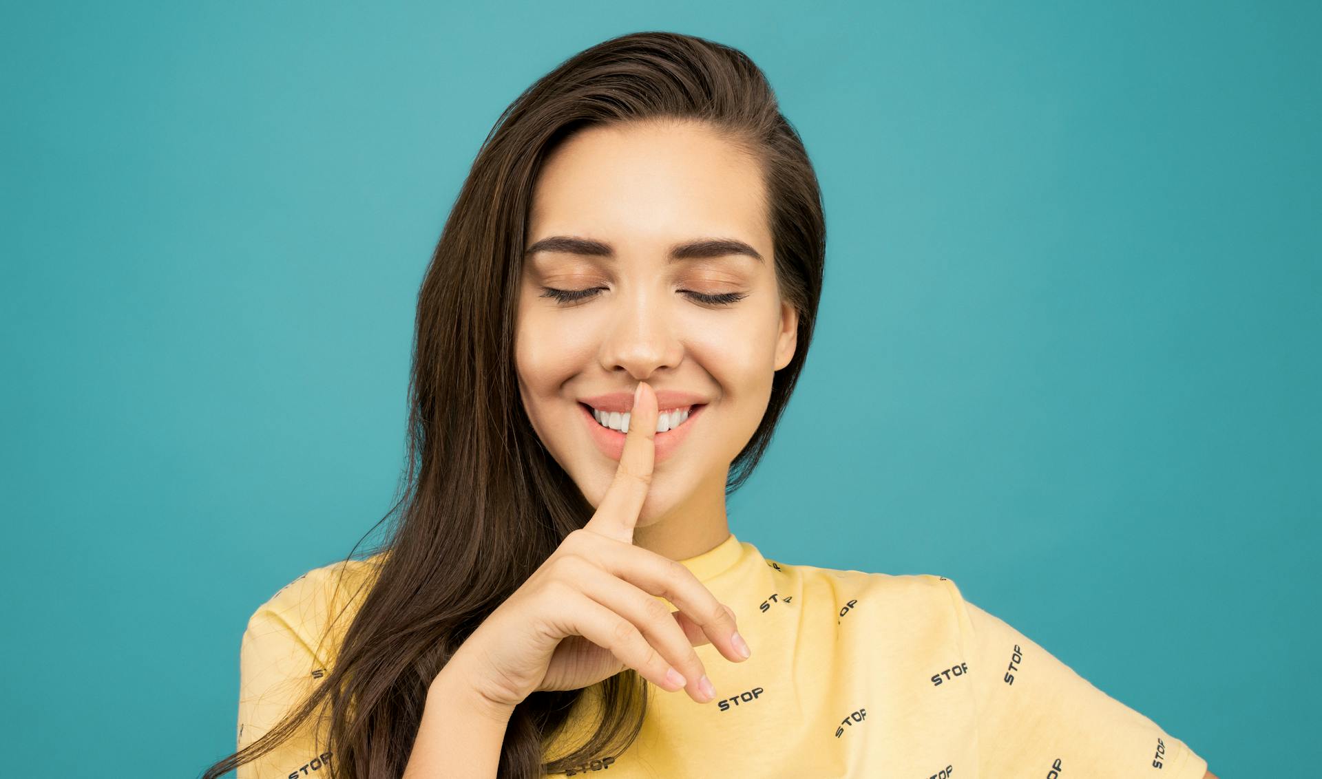 Une femme souriante avec un doigt pressé contre ses lèvres | Source : Pexels