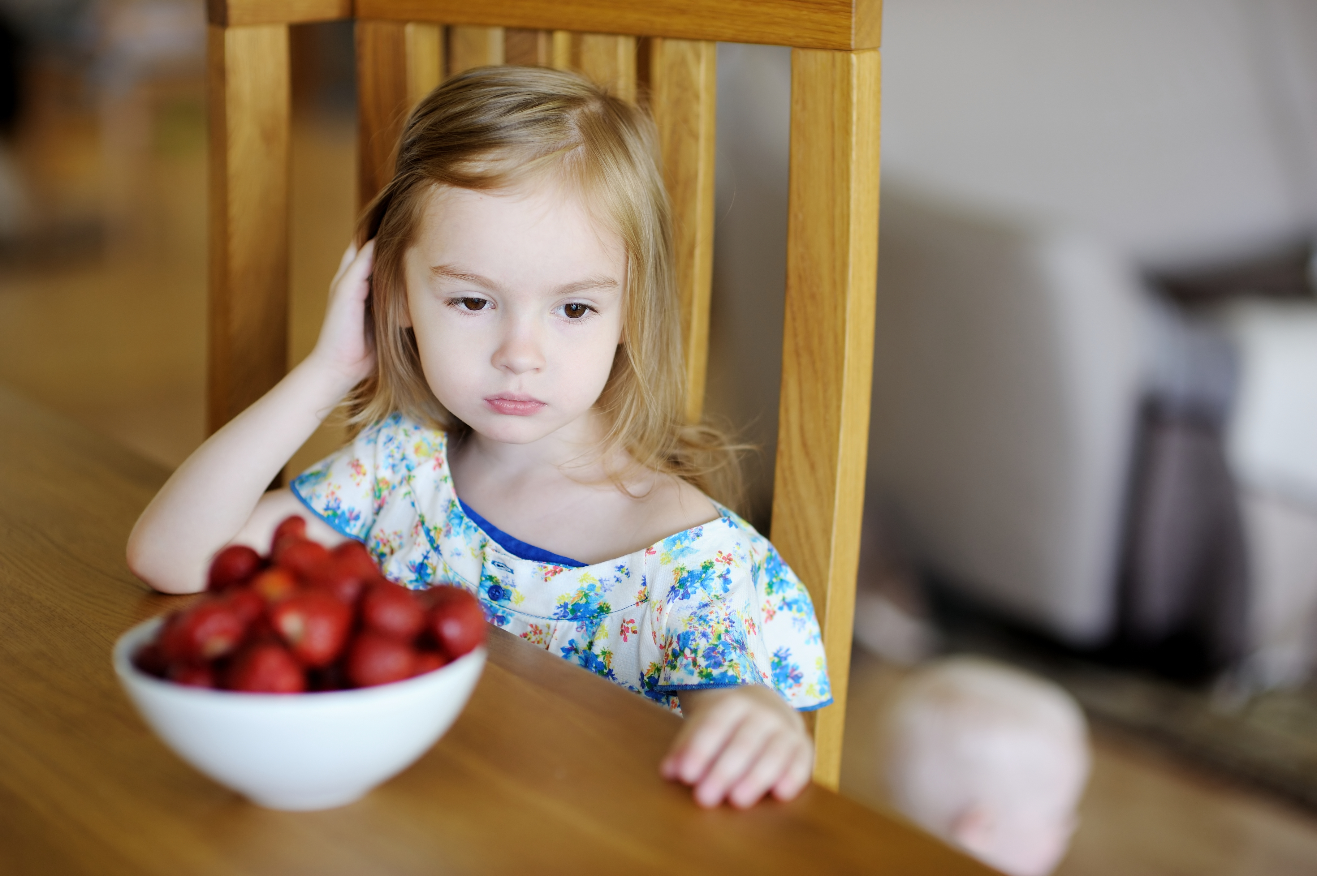 Petite fille à l'air triste avec un bol de fraises devant elle à la table à manger | Source : Shutterstock
