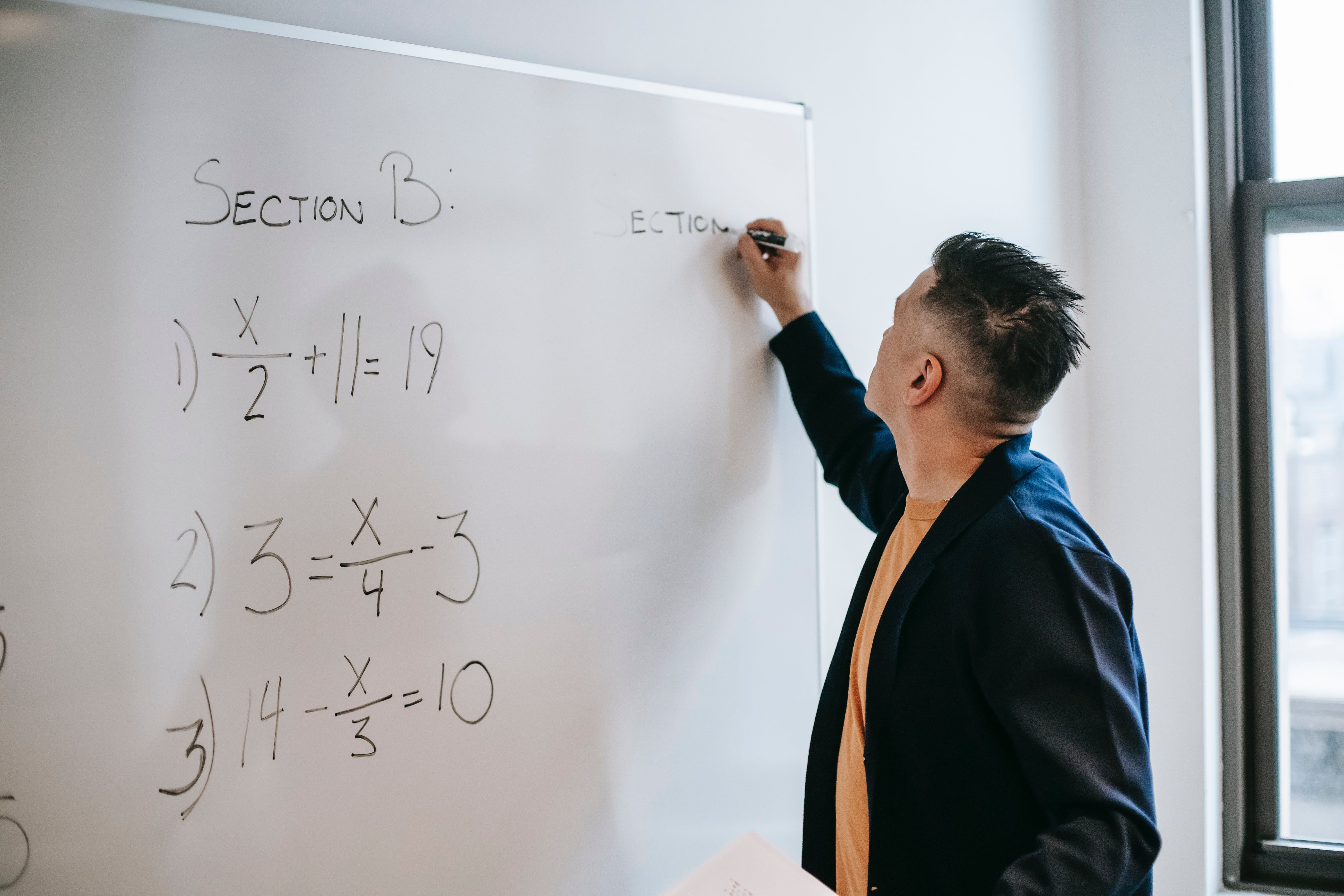 A man writing calculations on a whiteboard. | Source: Pexels