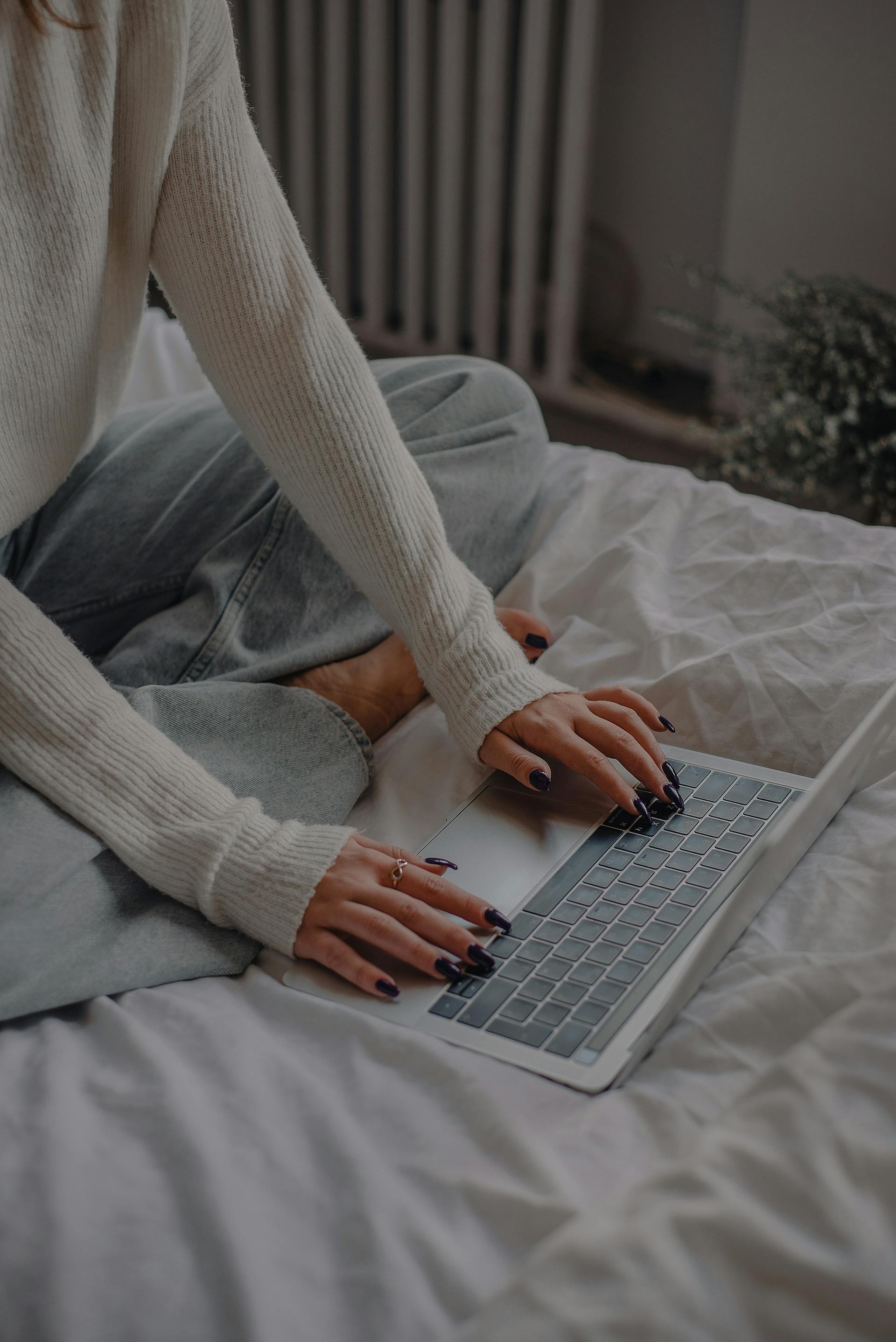 Une femme assise sur le lit et utilisant un ordinateur portable | Source : Pexels