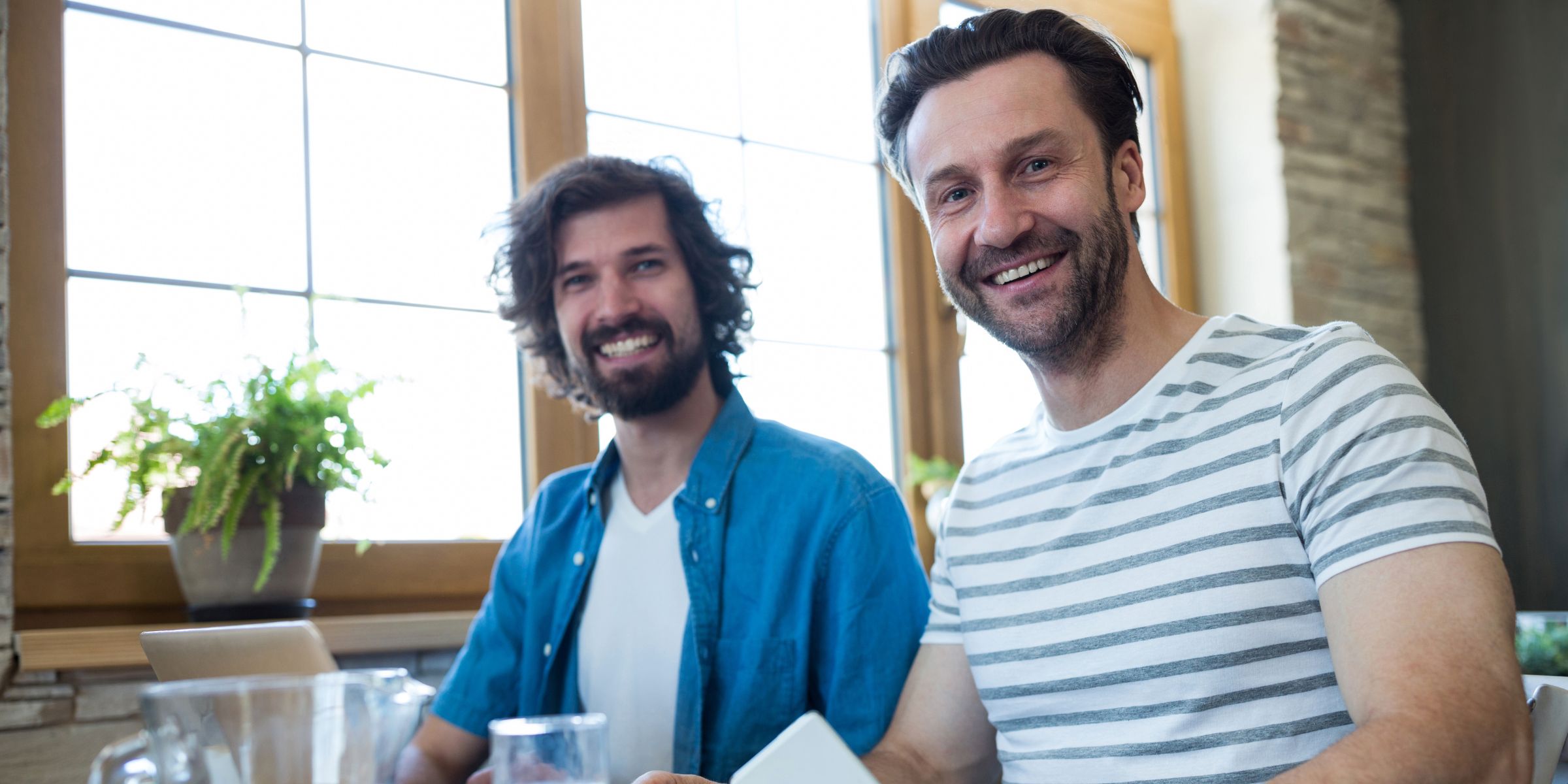 Deux hommes tout souriants, assis à une table | Source : Magnific