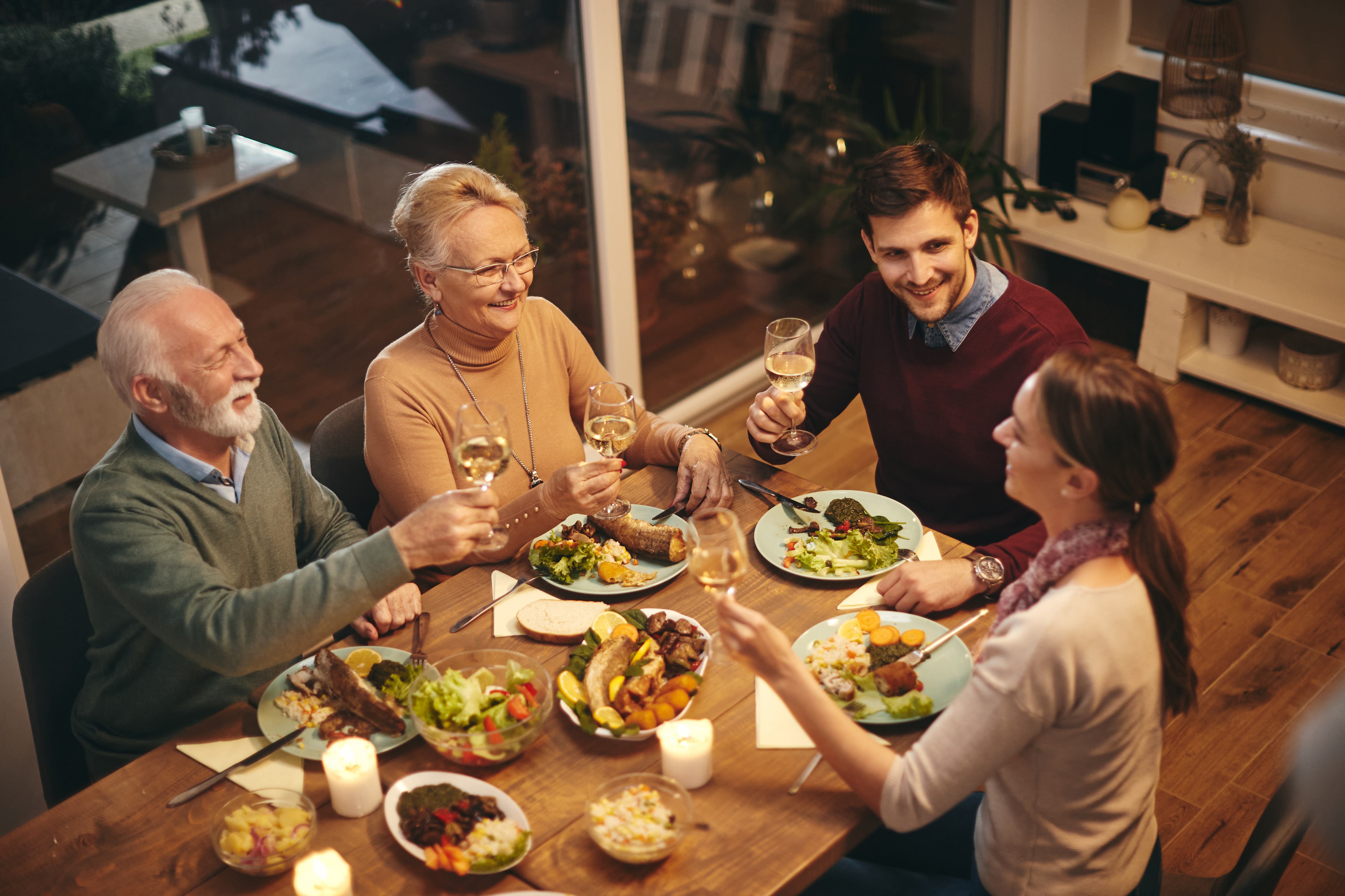 Une femme âgée heureuse trinque avec sa famille tout en prenant un repas à la table à manger | Source : Shutterstock