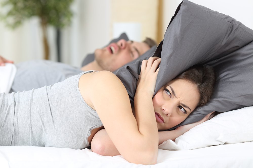 Un homme qui ronfle tandis que sa femme se couvre les oreilles avec son oreiller. | Shutterstock