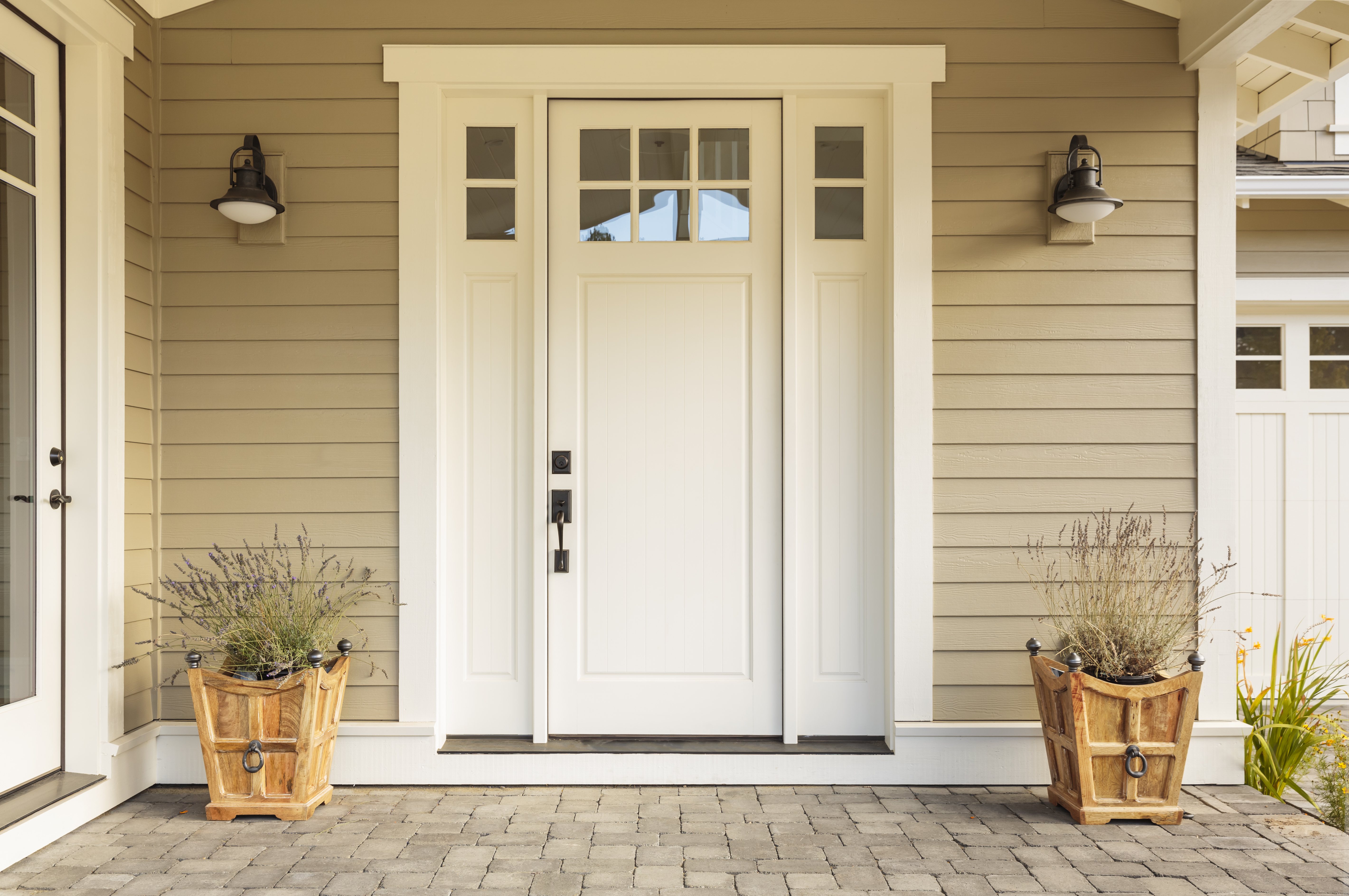 Porte d'entrée blanche avec de petites fenêtres décoratives carrées et des pots de fleurs | Source : Shutterstock
