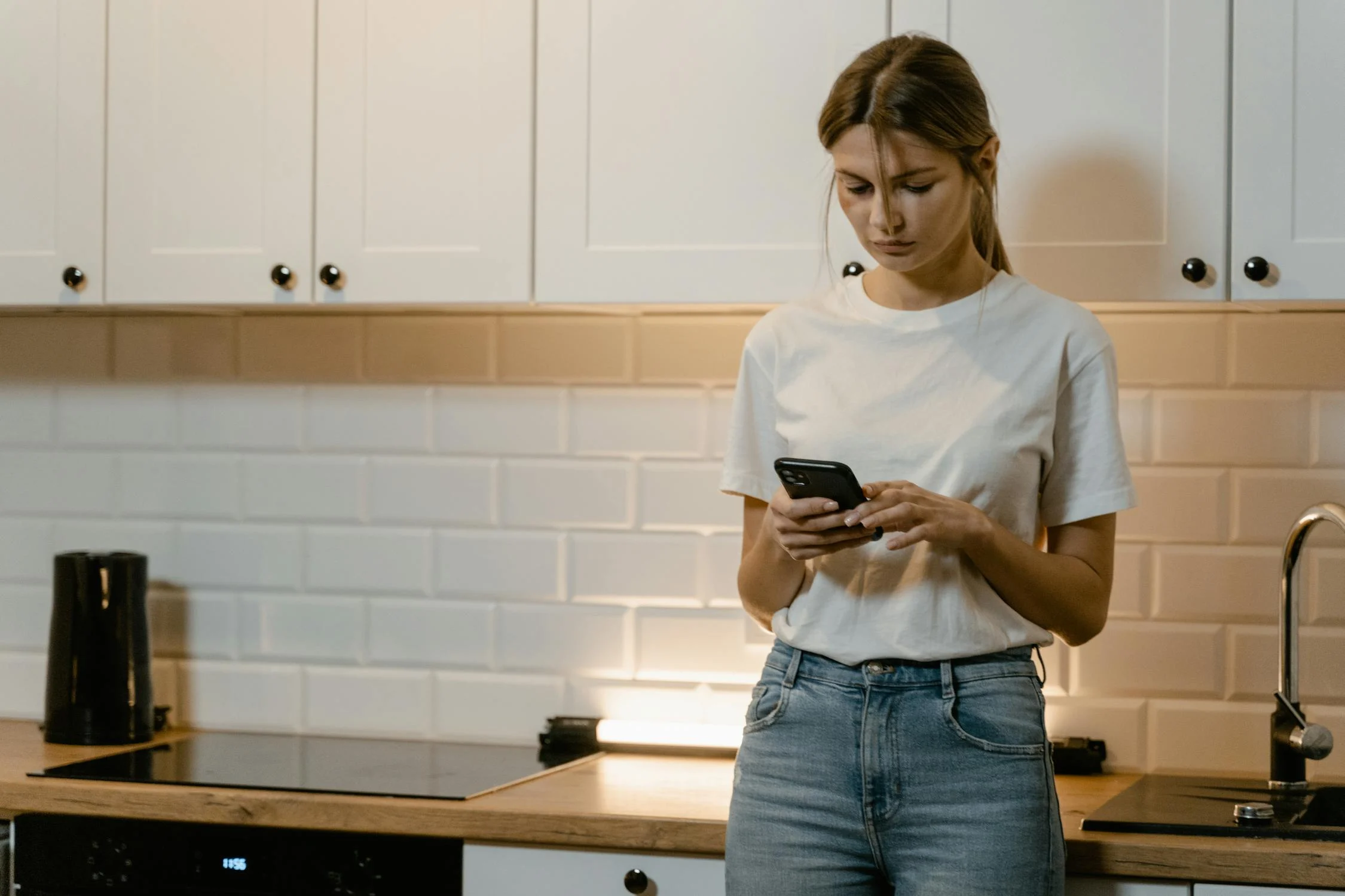 Une femme tapant sur son téléphone dans sa cuisine | Source : Pexels