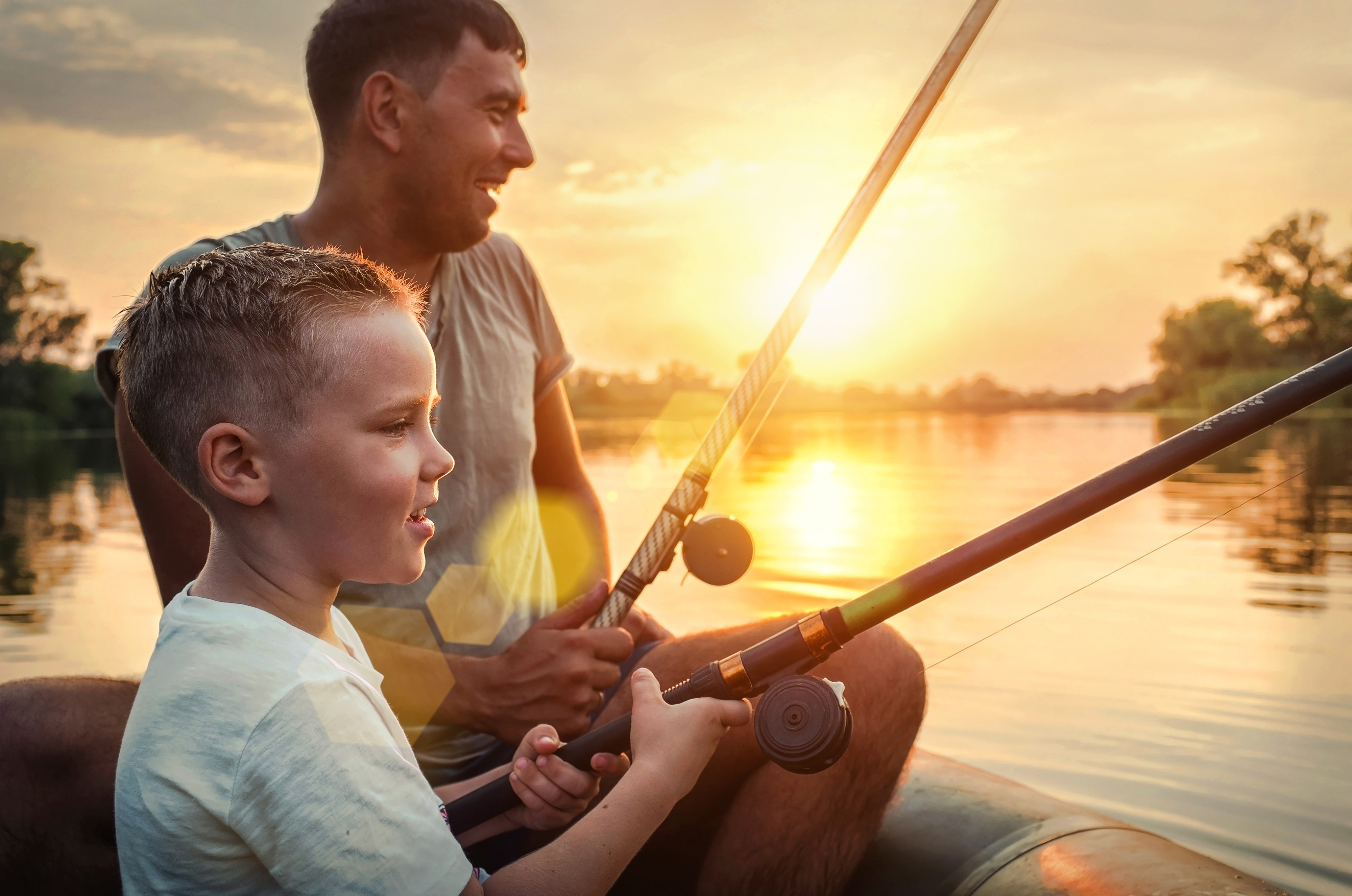 Père et fils pêchant ensemble depuis un canot pendant le coucher du soleil | Source : Shutterstock