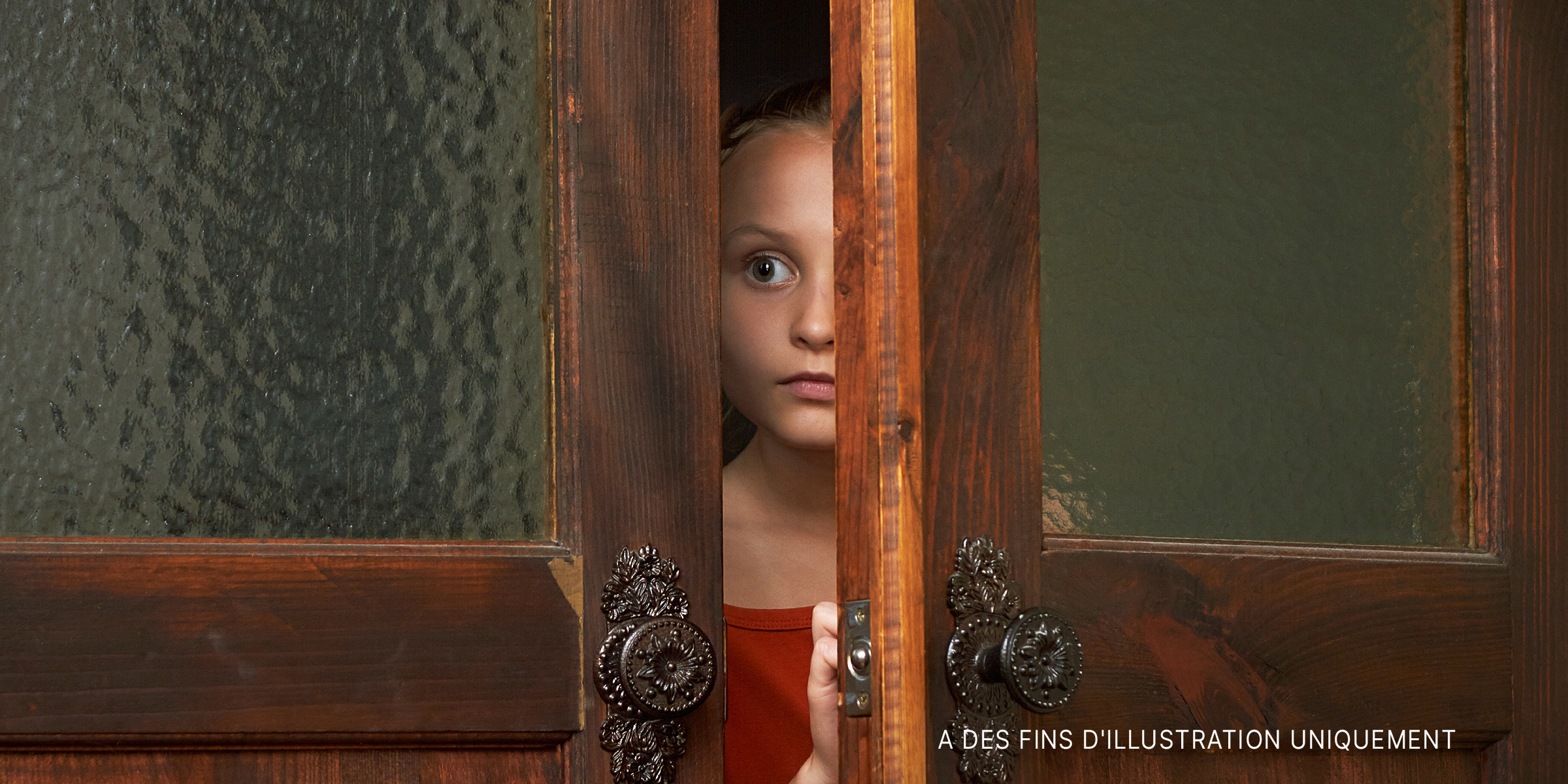 Une petite fille effrayée qui regarde par la fente de la porte | Source : Shutterstock