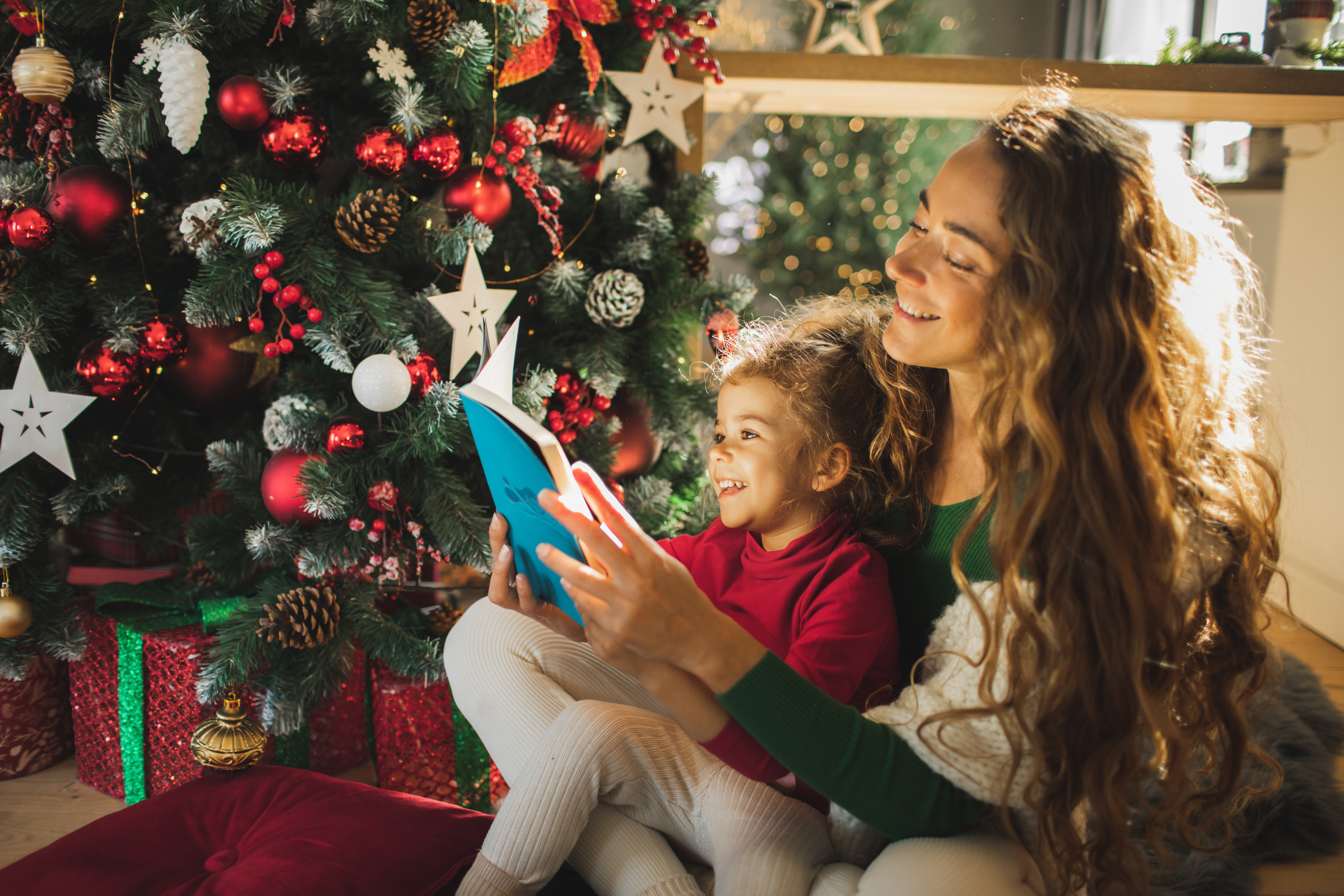 Une jeune mère lisant un livre à sa fille près d'un arbre de Noël | Source : Getty Images