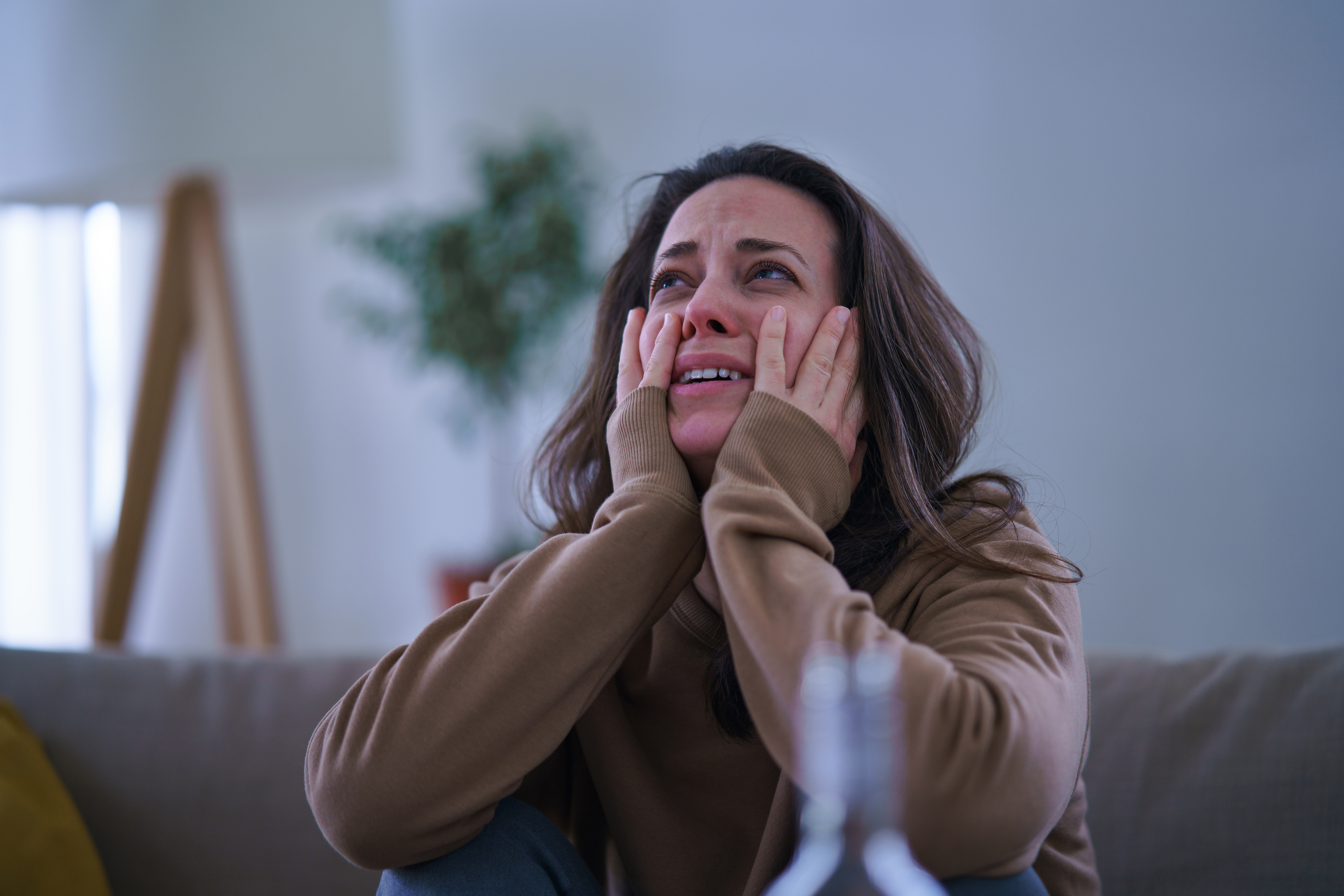 Une femme triste et déprimée en train de pleurer, assise à l'intérieur sur un canapé | Source : Getty Images