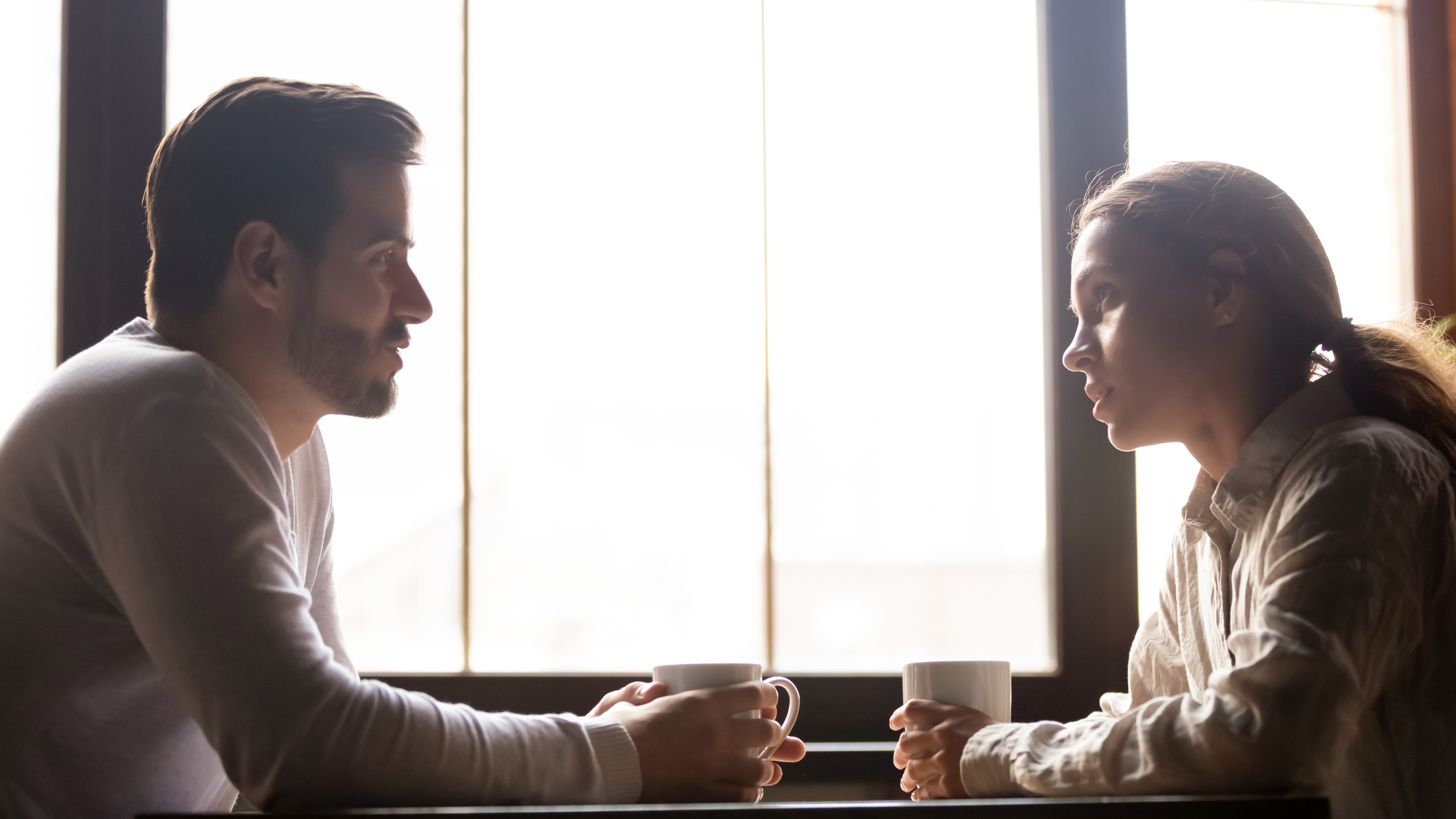Un homme et une femme assis l'un en face de l'autre, chacun tenant une tasse | Source : Shutterstock