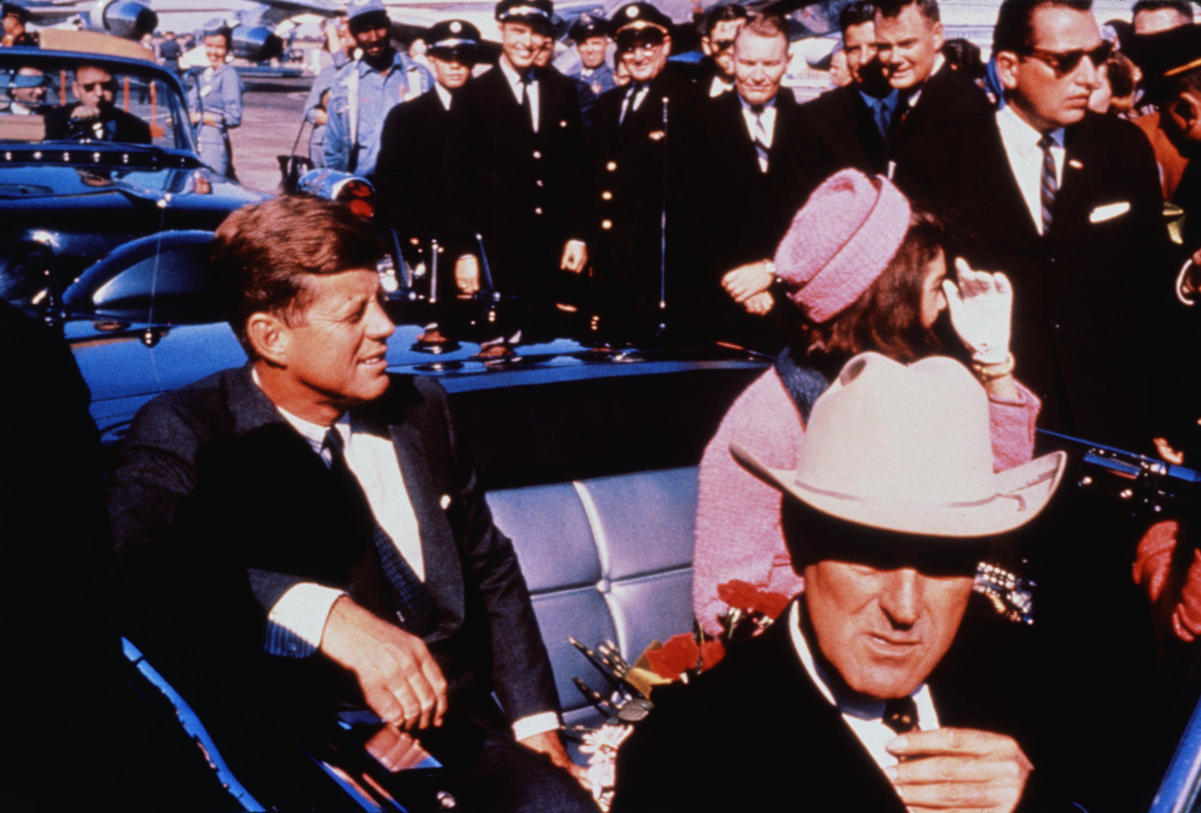 Le gouverneur du Texas John Connally ajuste sa cravate (au premier plan) alors que le président américain John F Kennedy (à gauche) et la première dame Jacqueline Kennedy (en rose) s'installent sur les sièges arrière, le 22 novembre 1963 | Source : Getty Images