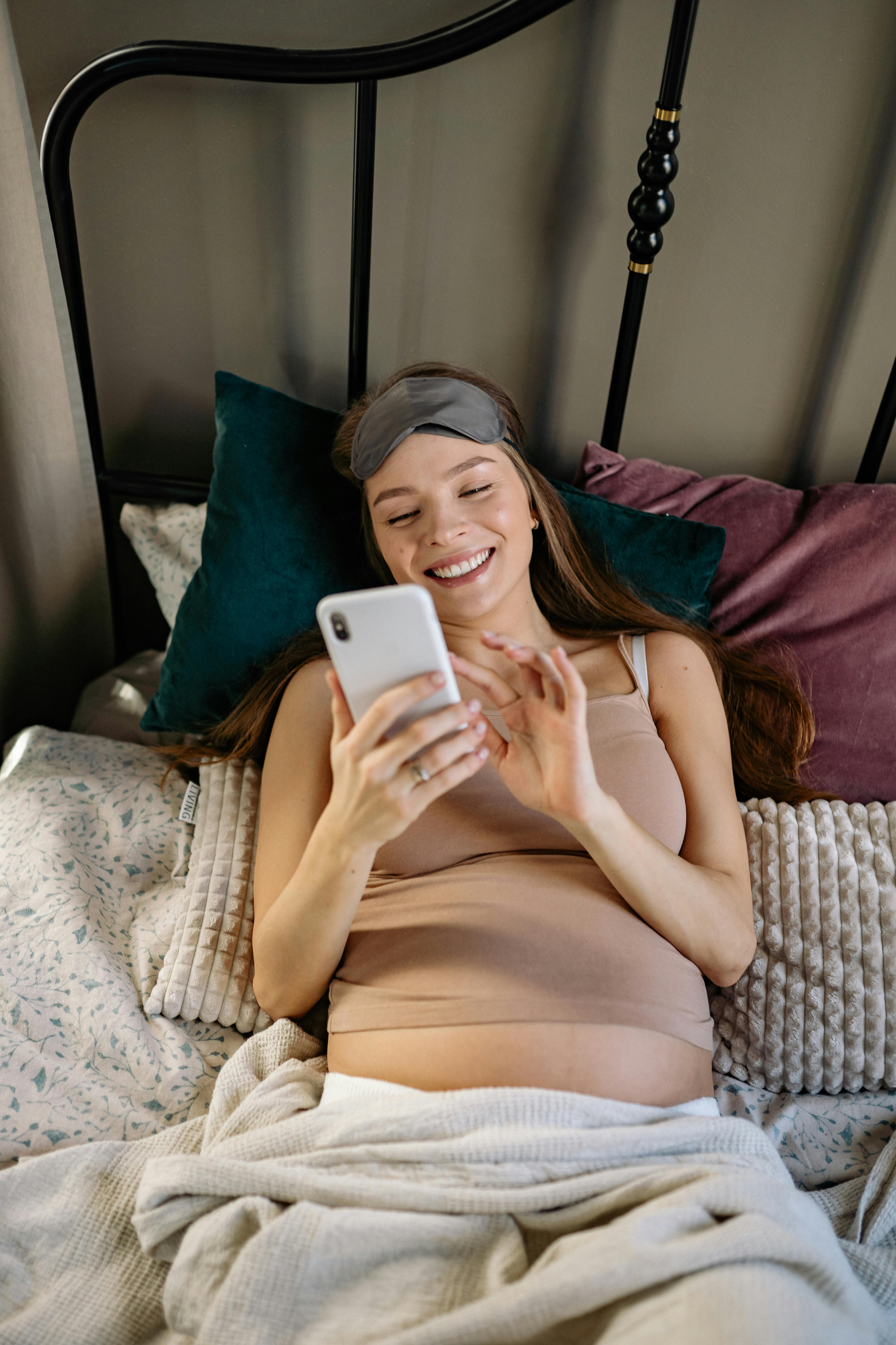 Une femme enceinte souriante lisant son téléphone au lit | Source : Pexels