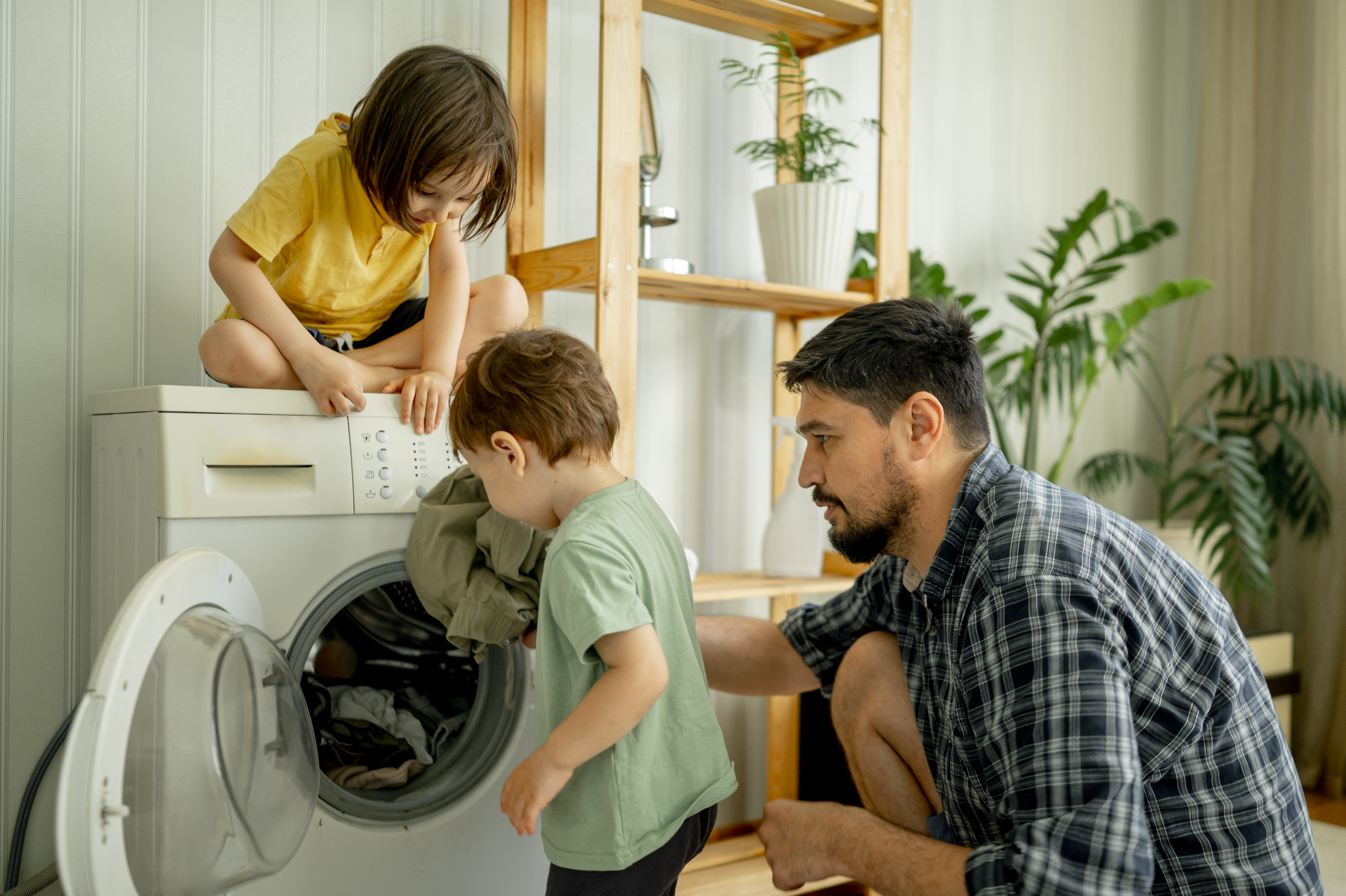 Père et enfants mettant des vêtements dans la machine à laver | Source : Getty Images