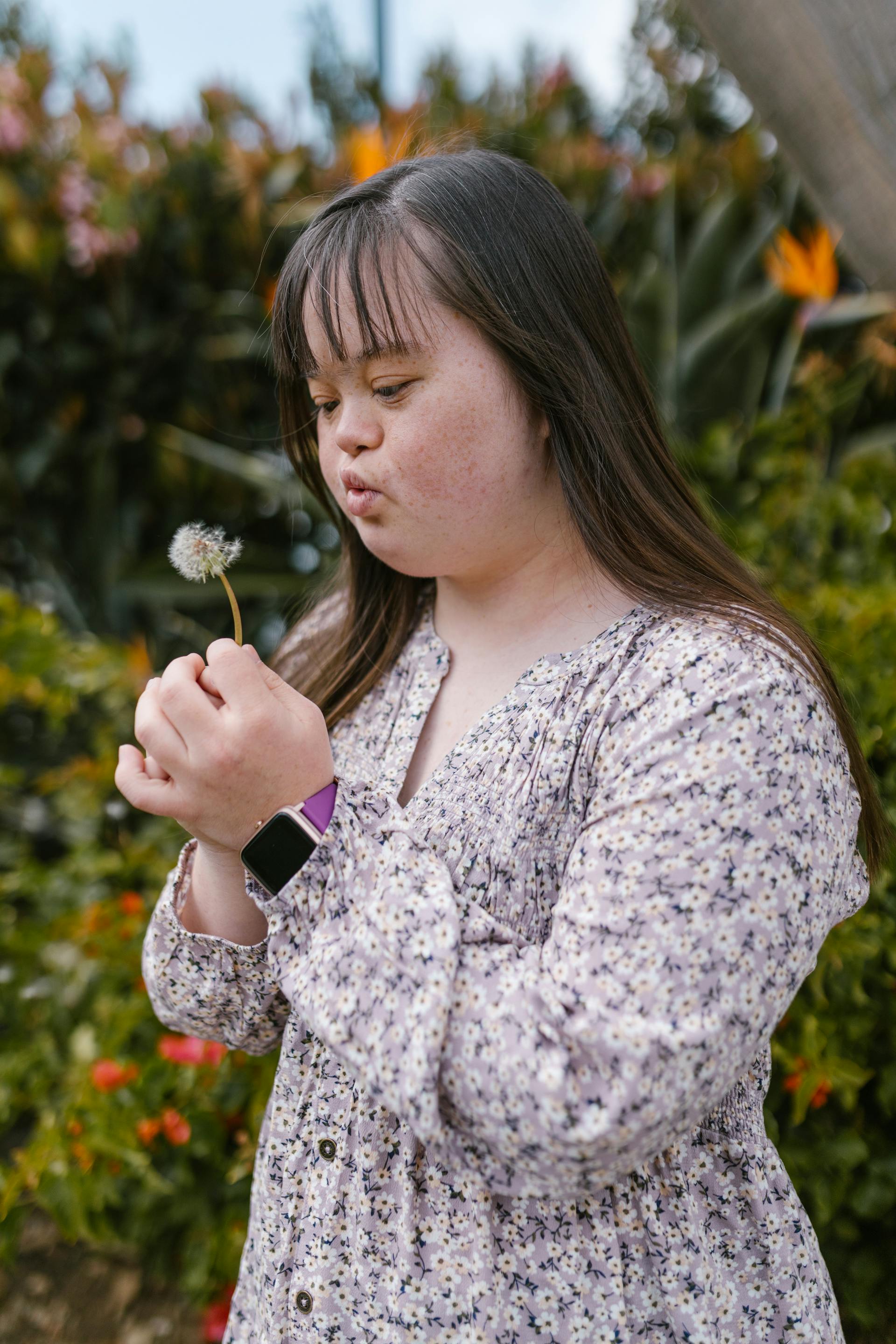 Une fille atteinte du syndrome de Down tient un pissenlit blanc | Source : Pexels
