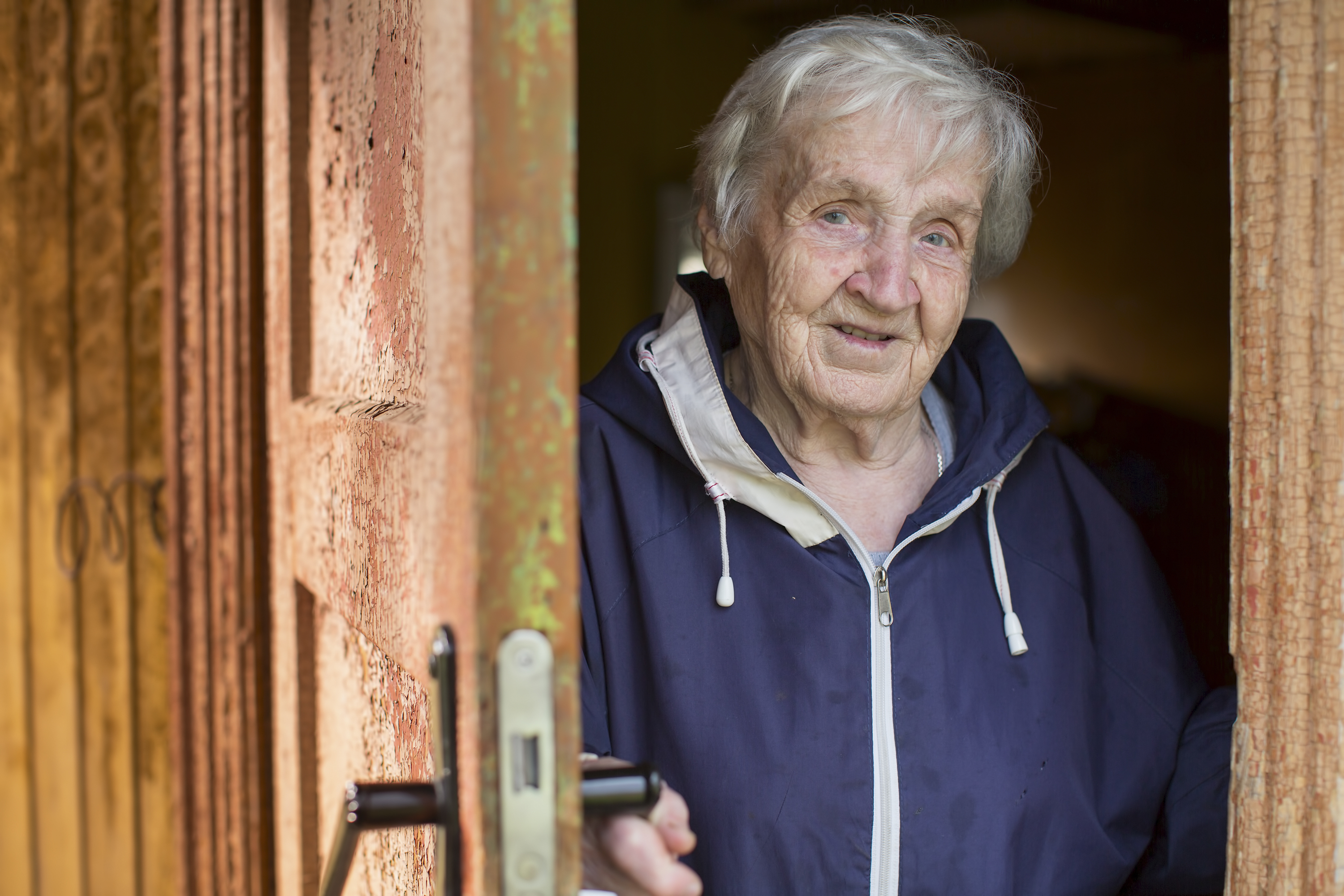 Una anciana se asoma desde detrás de la puerta de su casa. | Fuente: Shutterstock