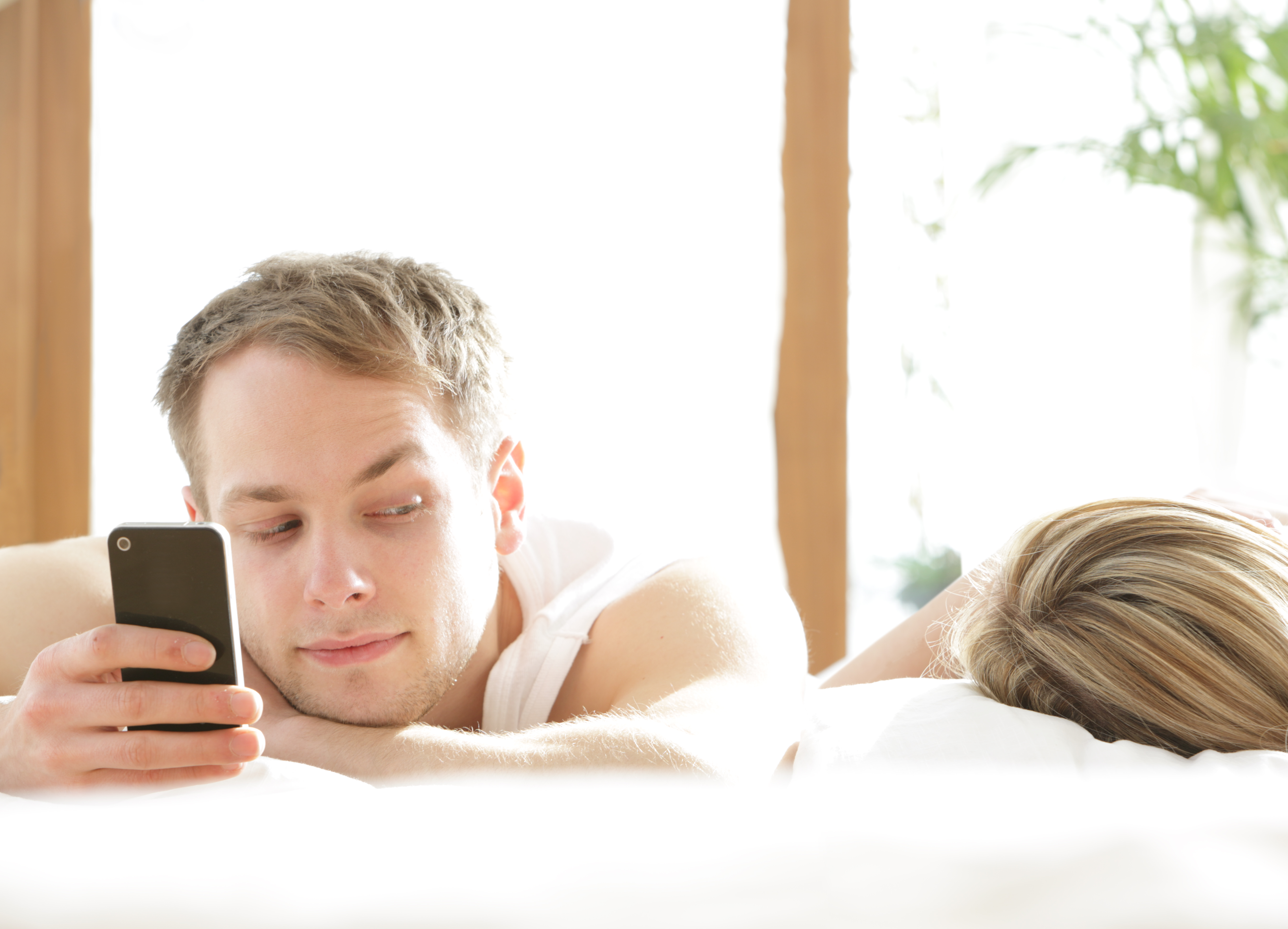 Homme avec un téléphone dans le lit, regardant une femme endormie | Source : Getty Images