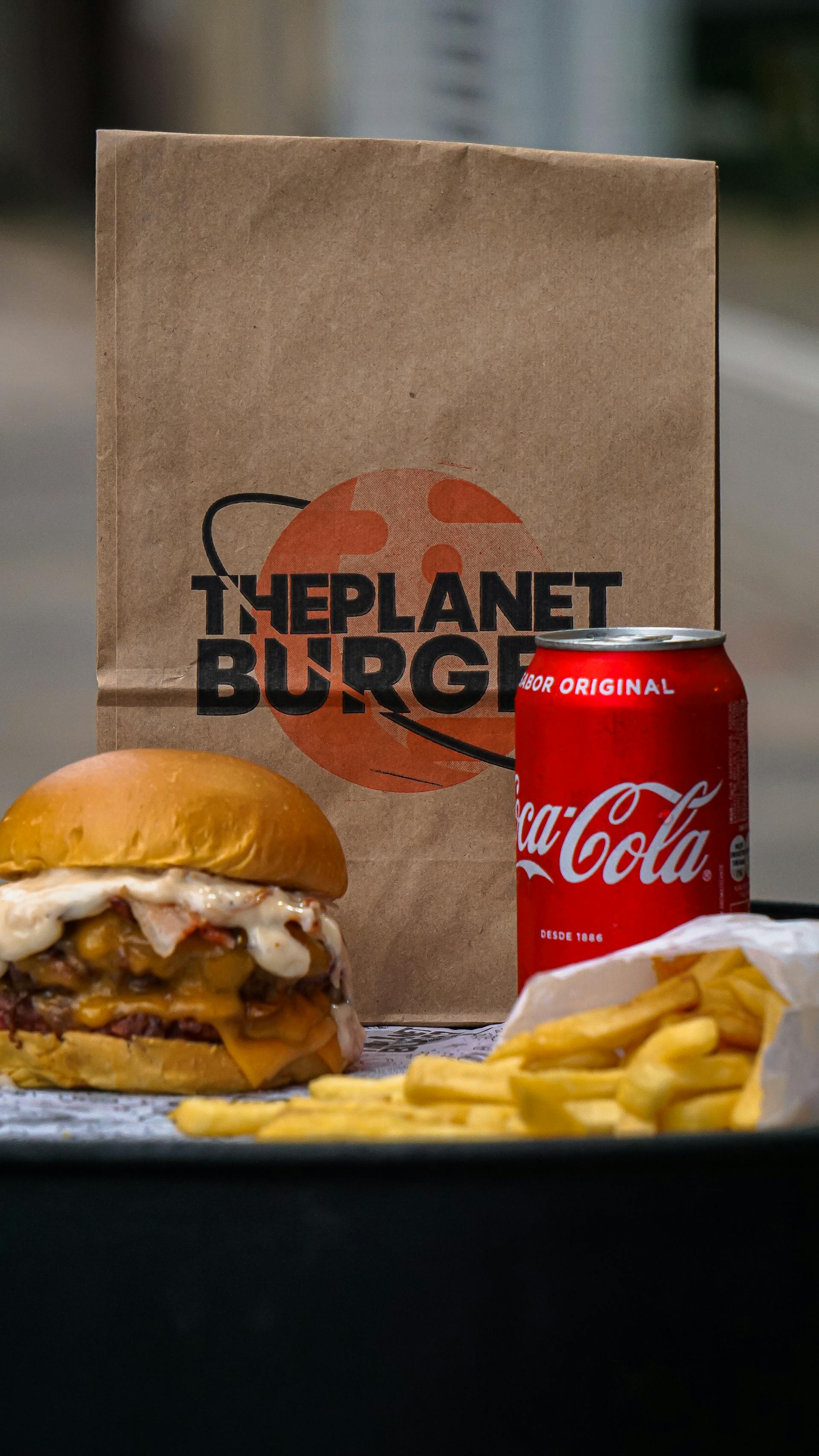 Un hamburger, des frites et une canette de soda posés à côté d'un sac en papier | Source : Pexels