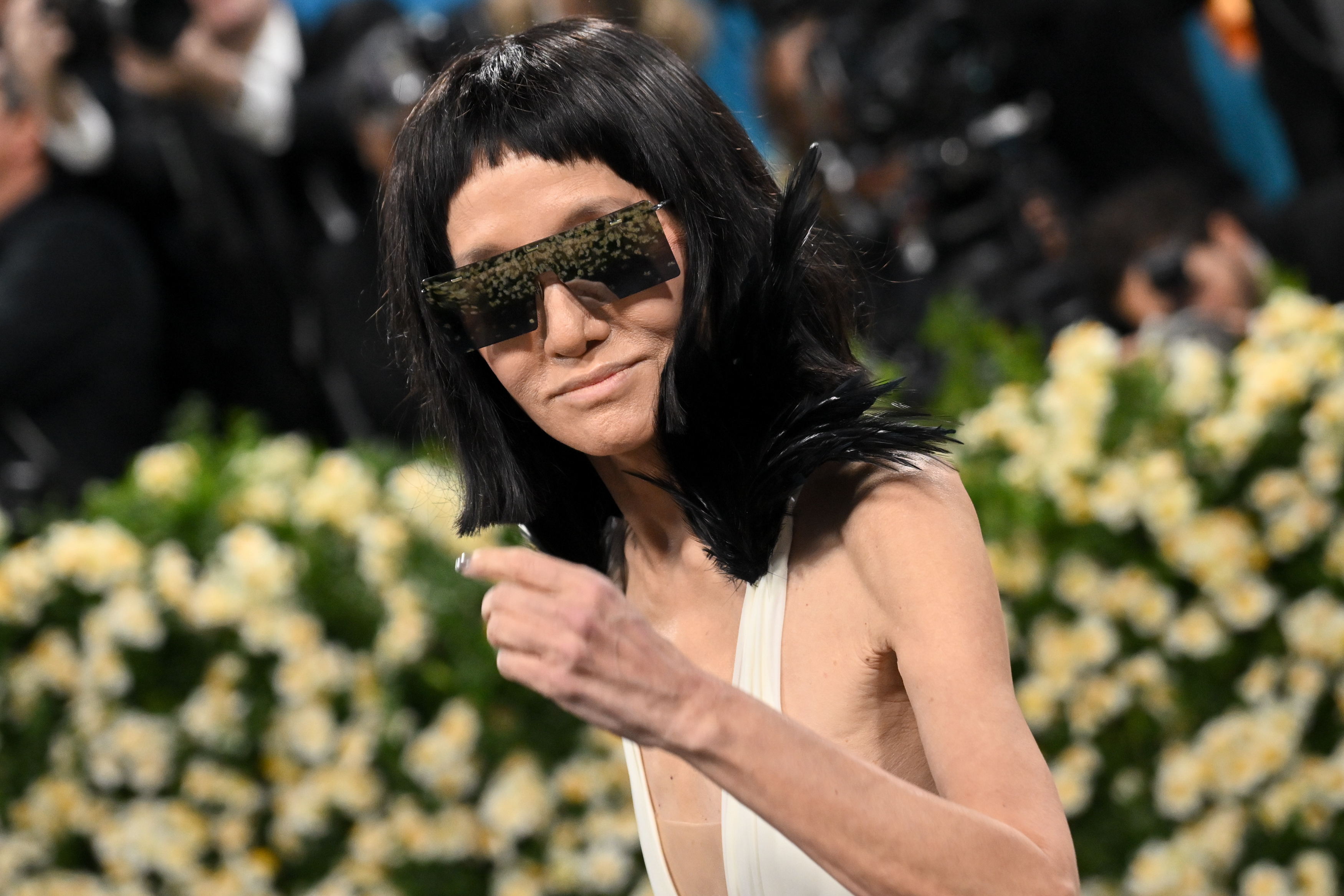 Dans un moment candide, Vera Wang fait un geste à la foule tandis que ses lunettes de soleil et son décolleté en plumes reflètent l'énergie de la soirée.