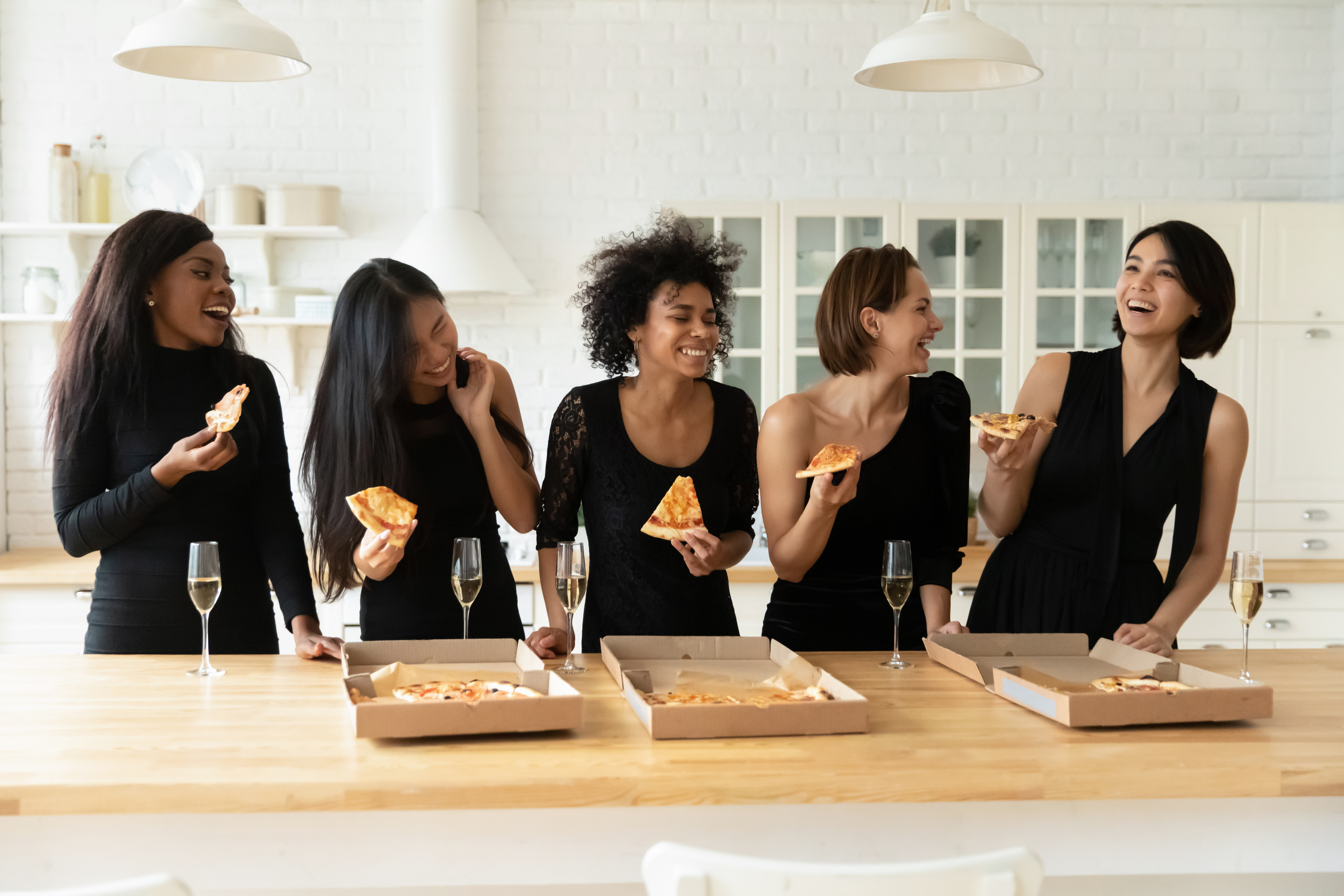 Des femmes vêtues de noir mangent des pizzas et boivent du champagne | Source : Shutterstock