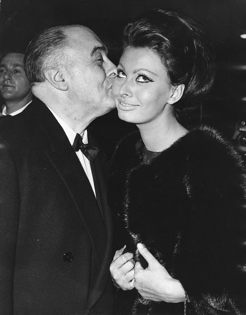 Le producteur de films italien Carlo Ponti embrasse sa femme, l'actrice Sophia Loren, après qu'elle ait reçu le premier prix Alexander Korda, la nommant "Star internationale de l'année", lors de la première mondiale de son nouveau film "Lady L" à l'Empire le 26 novembre 1965 | Source : Getty Images