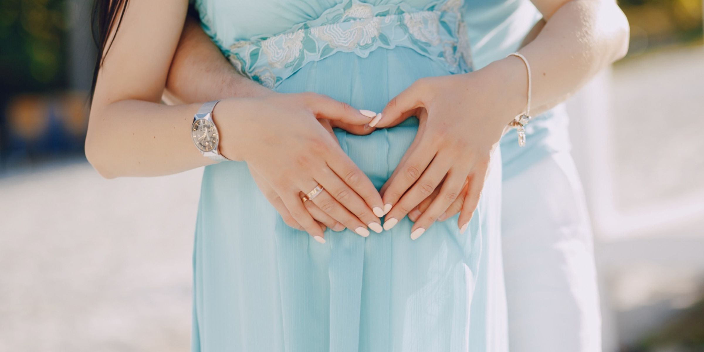 Gros plan sur un couple de futurs parents formant un cœur avec leurs mains au-dessus du ventre de la future maman | Source : Magnific