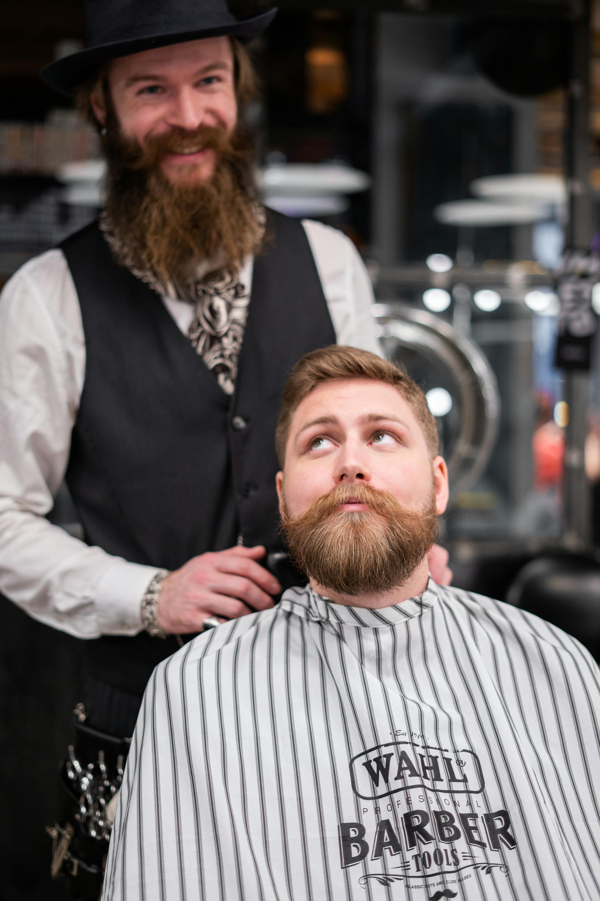 Un barbier sourit alors qu'il se tient derrière un client dans sa boutique | Source : Pexels