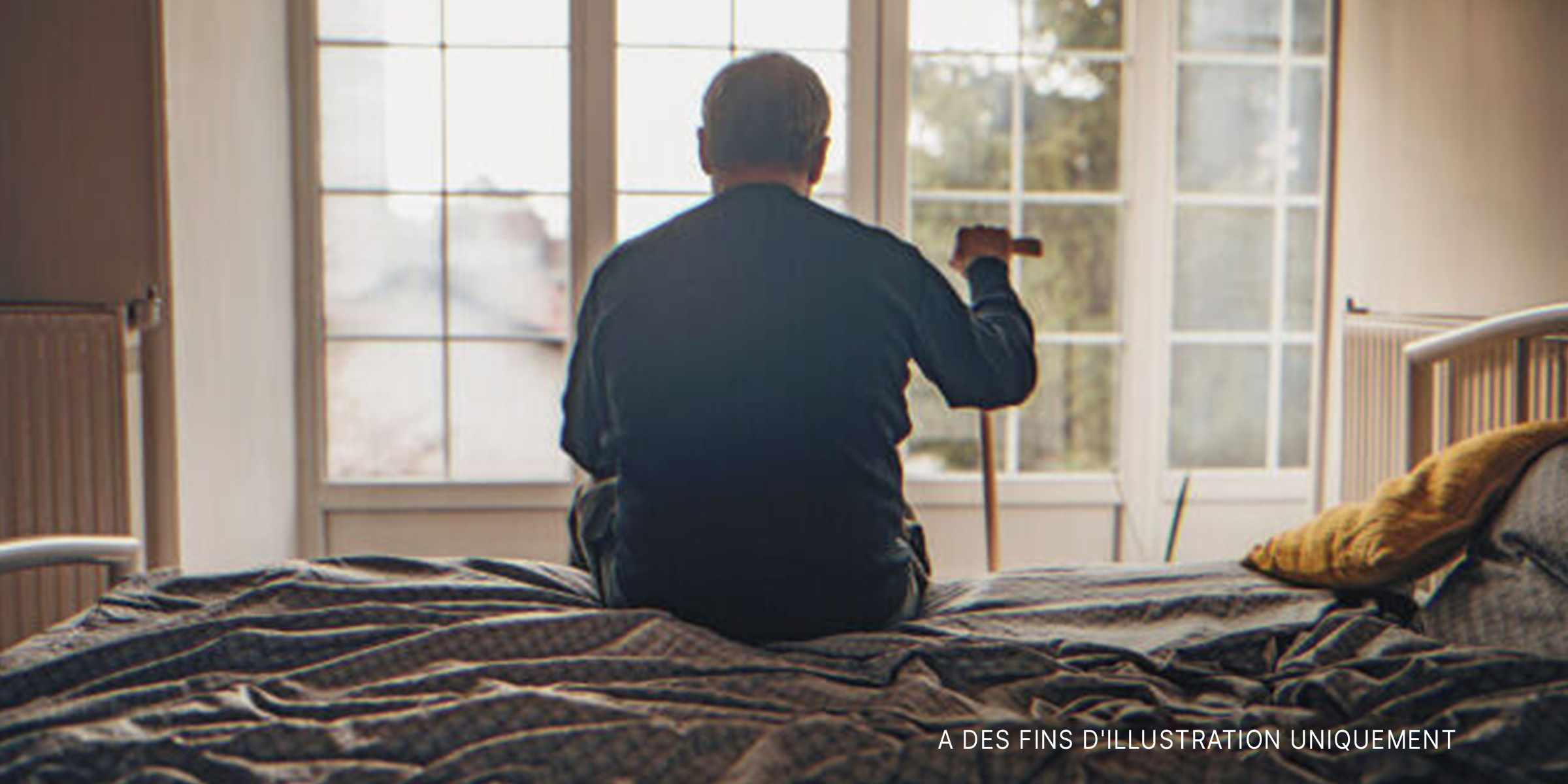Vieil homme assis dans un lit, regardant par la fenêtre | Source : Getty Images